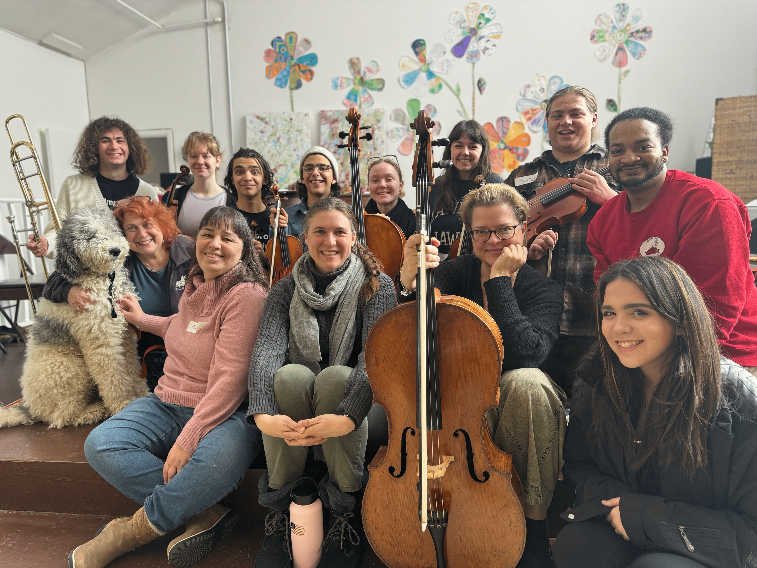 A smiling group of teachers holding various instruments including a cello in the front.