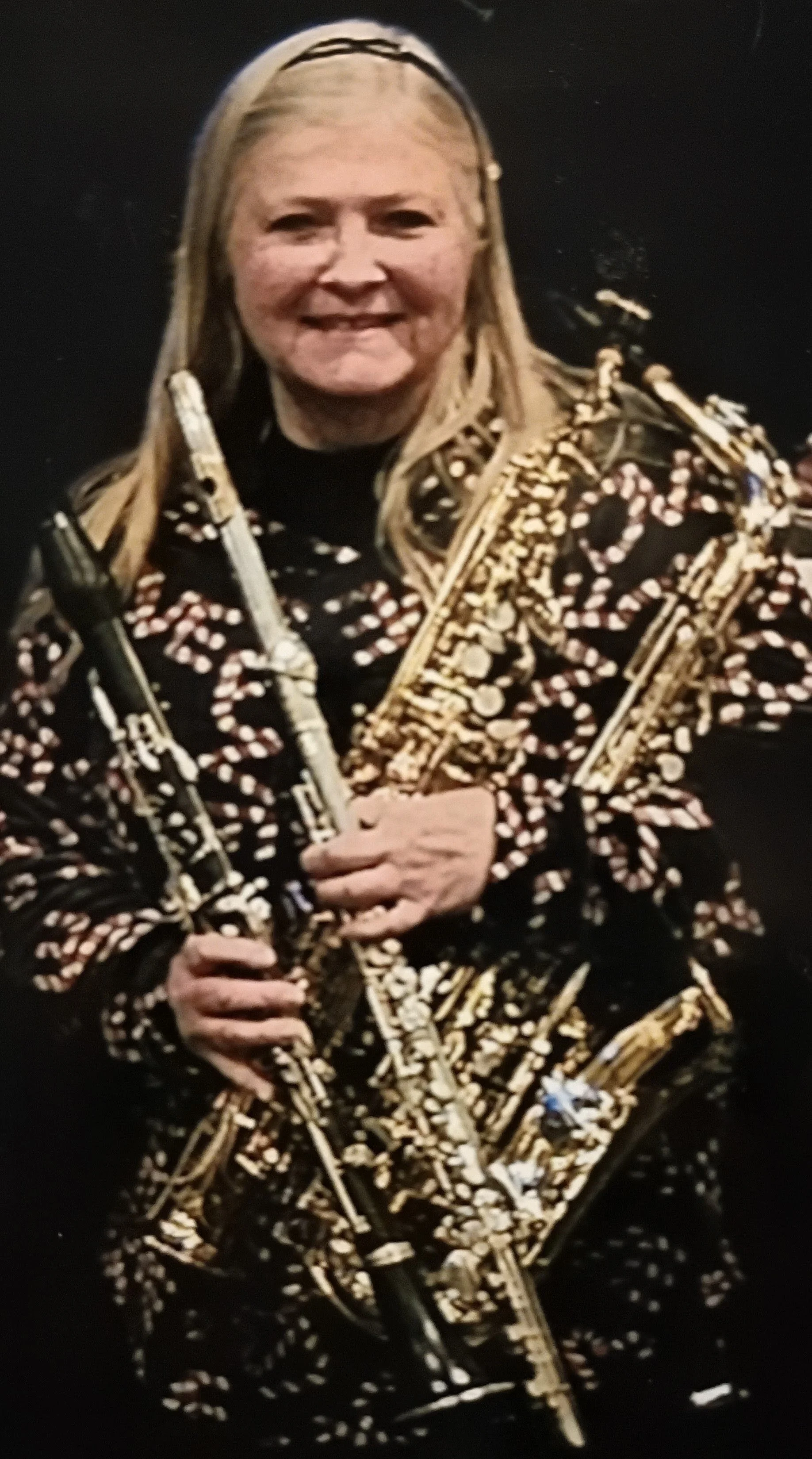 A smiling woman holds a clarinet, flute, and saxophone bundled together in her arms.
