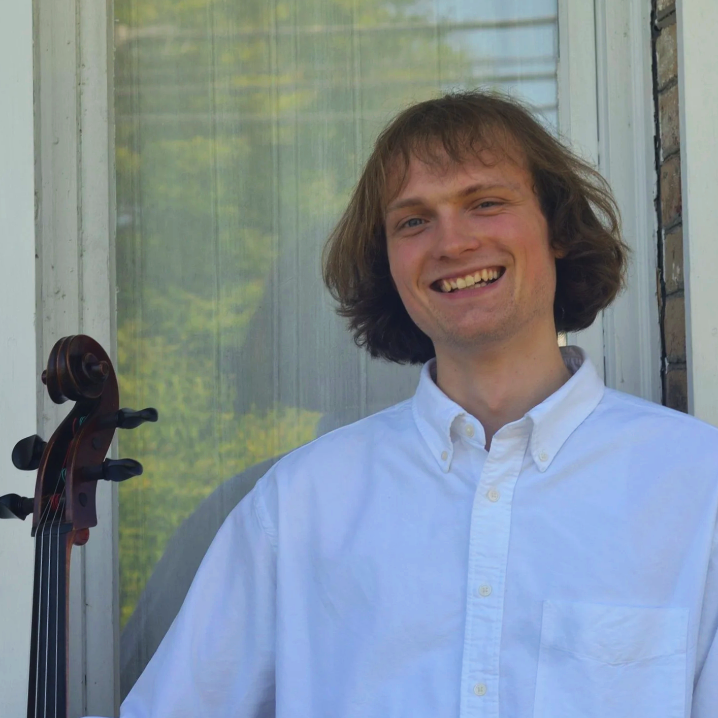 A smiling portrait photograph of a man with long hair holding a cello.