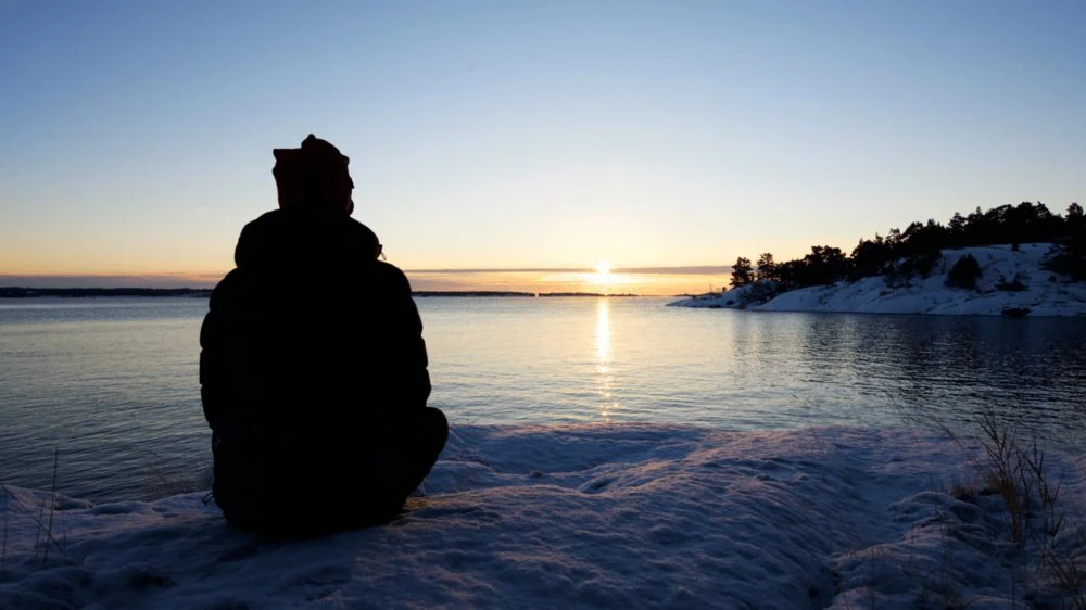 Person sitting on the edge of a lake in winter
