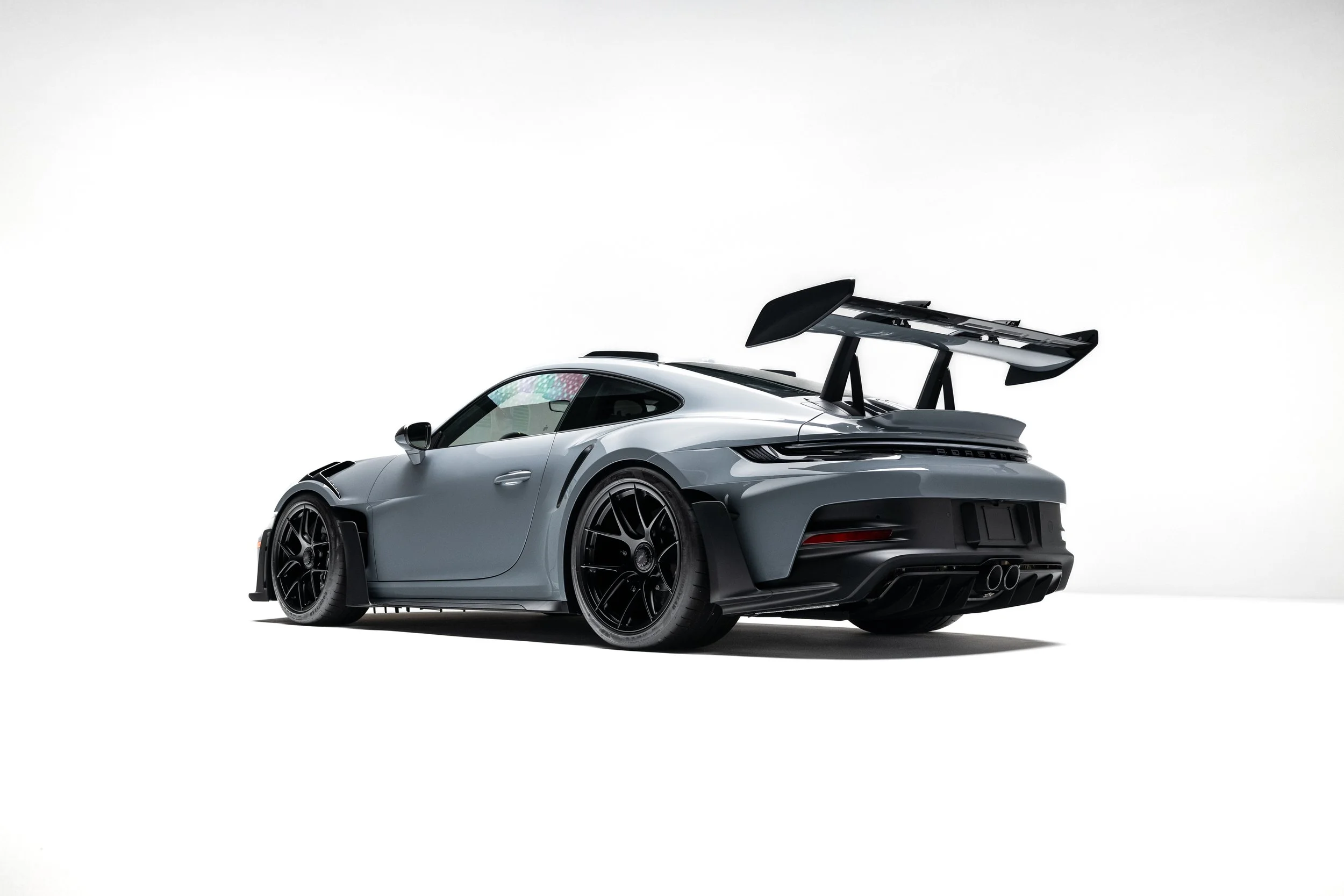 Rear three-quarter exterior view of a 2025 Porsche 911 GT3 RS in Arctic Grey, showing swan-neck rear wing, center-exit exhaust, diffuser, and black wheels.