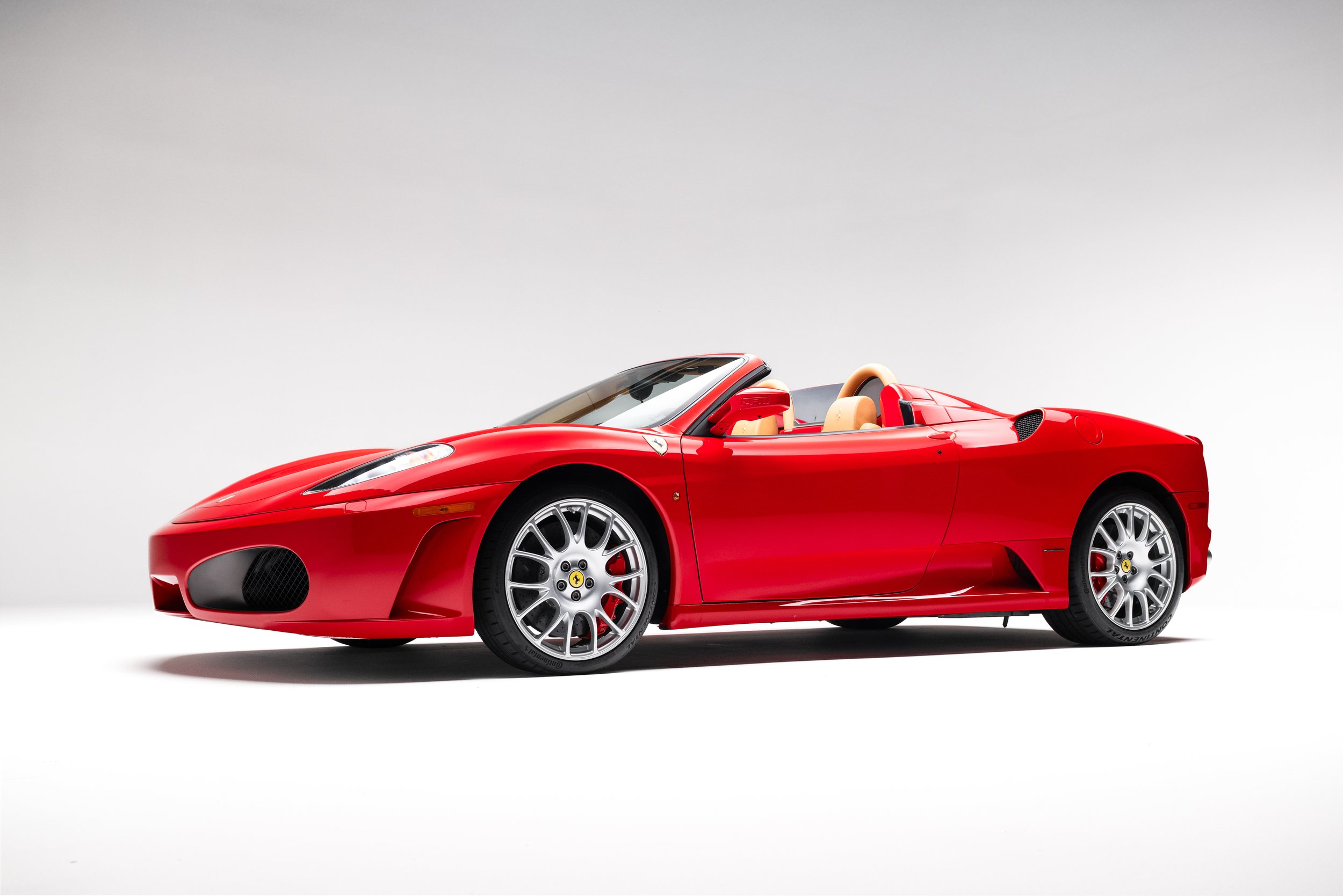 Side view of a red 2005 Ferrari F430 Spider with top down, showing alloy wheels and sculpted body lines.