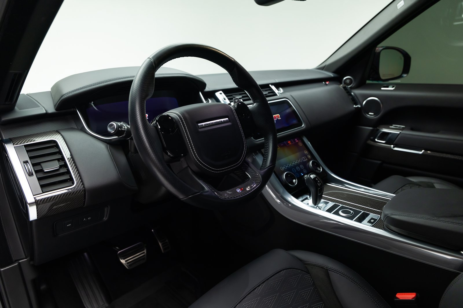 Black leather cockpit of the 2022 Range Rover Sport SVR, showing its steering wheel, digital instruments, center console, and carbon-fiber trim.