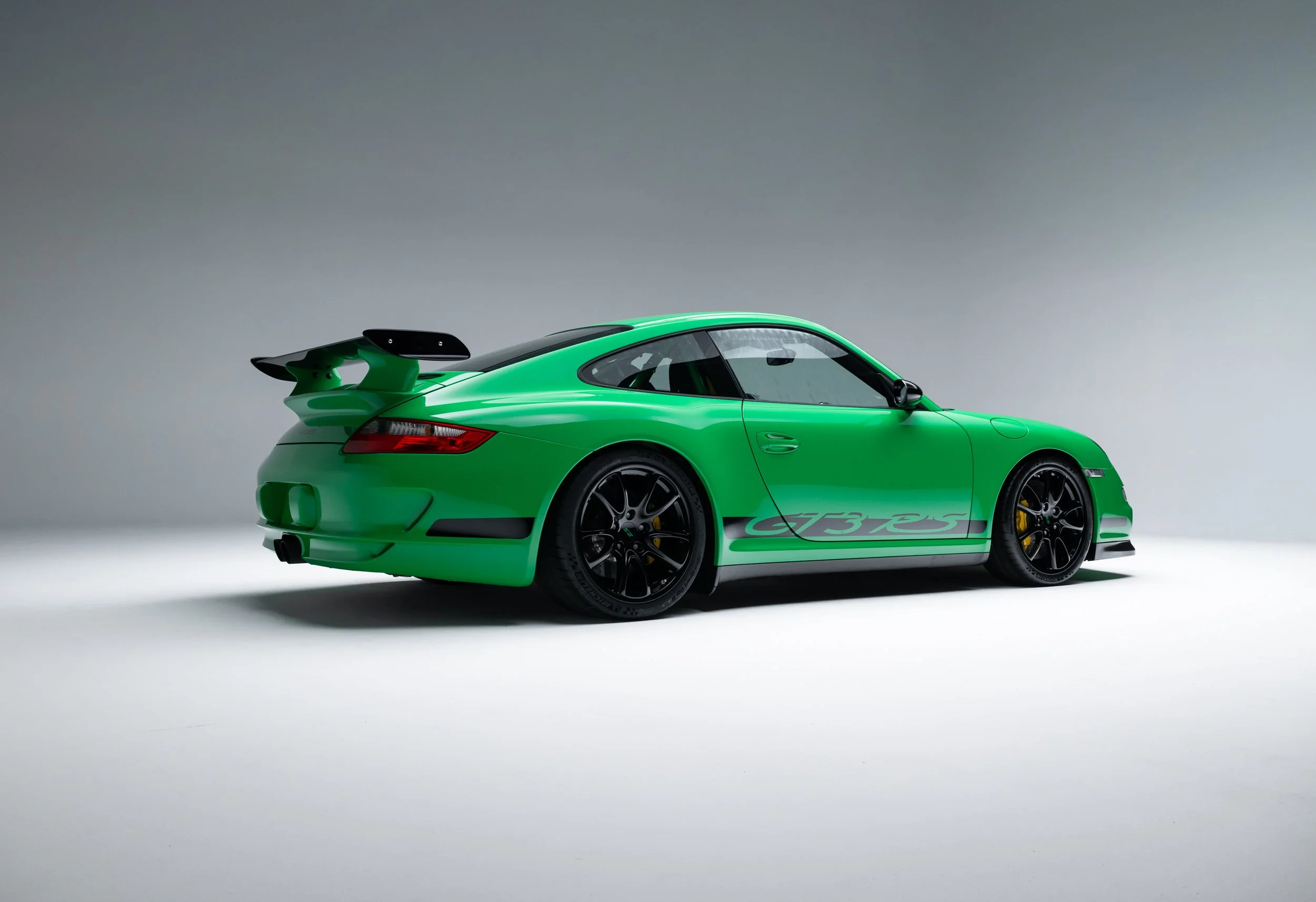 Rear 3/4 view of a green 2008 Porsche 911 GT3 RS with large rear wing, black multi-spoke wheels, side GT3 RS graphics, and rear diffuser.