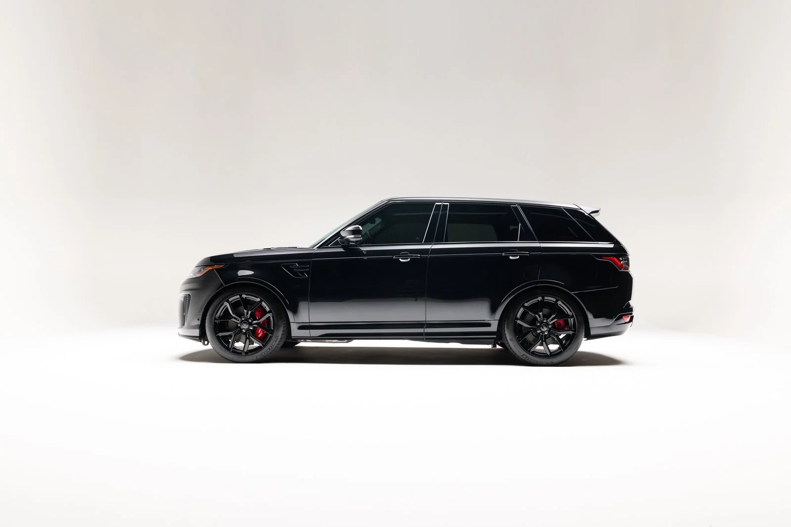 Side-profile studio view of the black 2022 Range Rover Sport SVR with black wheels and red brake calipers.