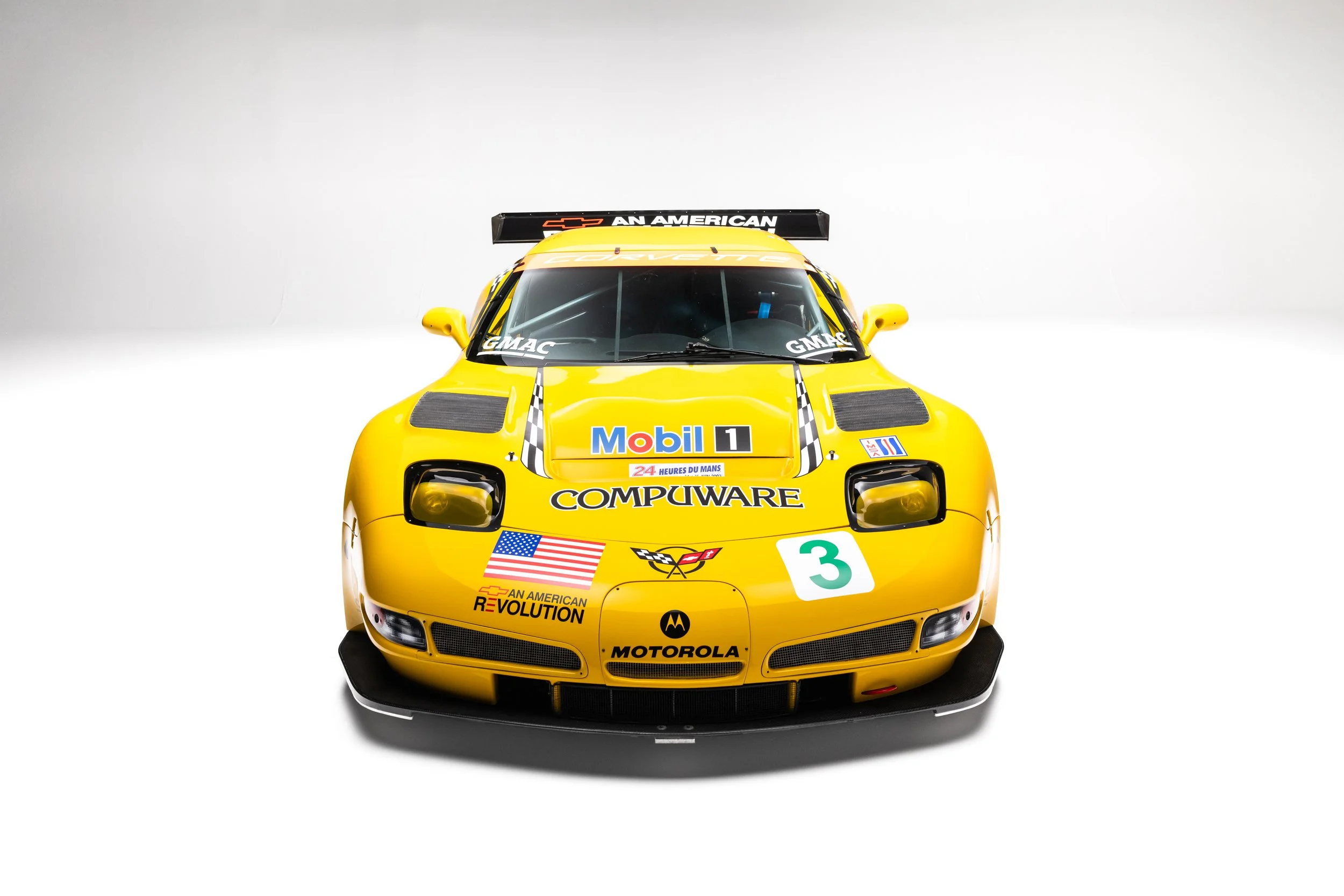 Chevrolet Corvette C5-R in yellow livery, featuring prominent front splitter, fixed headlights, and racing decals. The vehicle is positioned head-on, showcasing its aerodynamic design and sponsor logos.