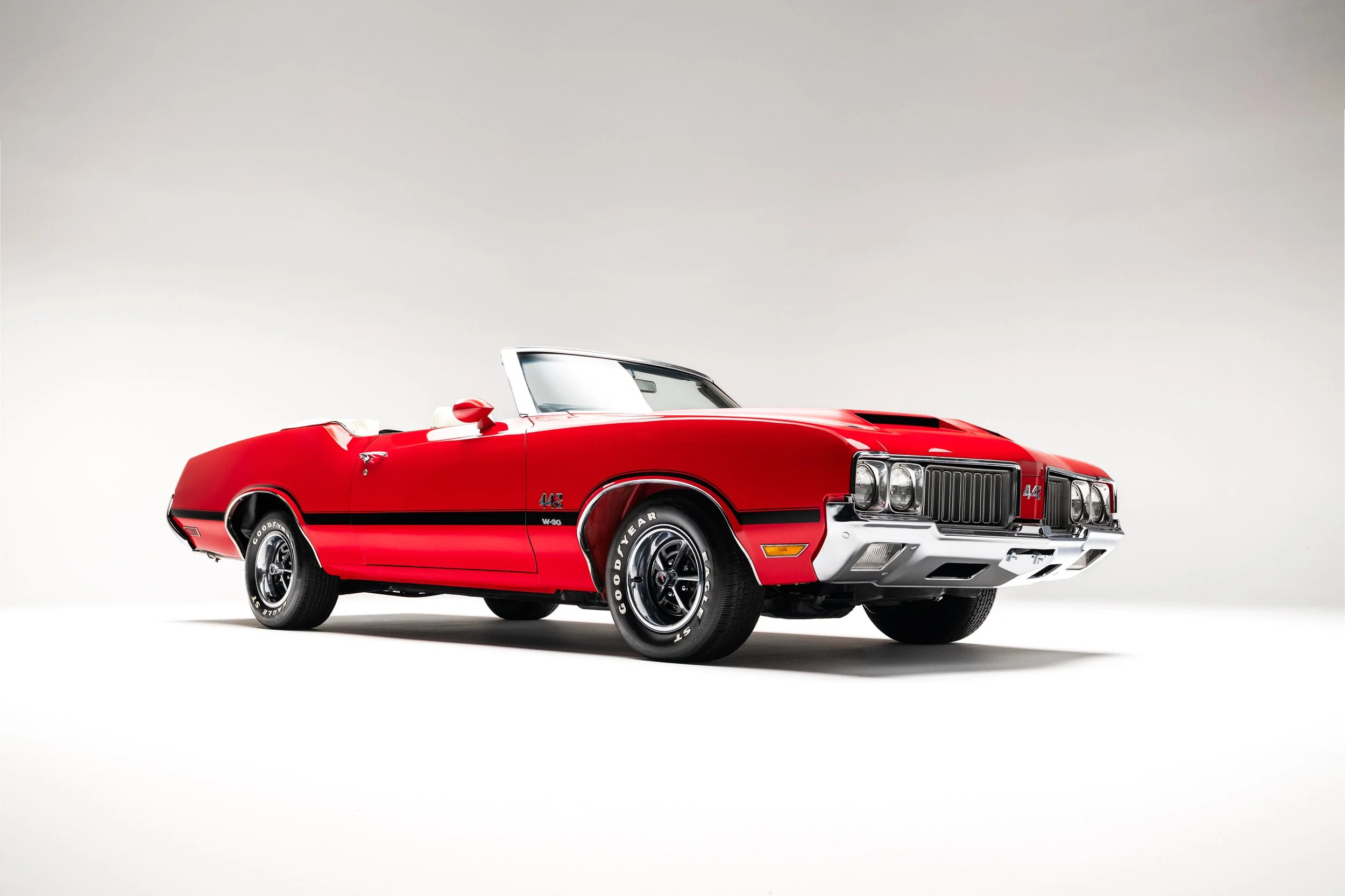 Front 3/4 exterior view of a red 1970 Oldsmobile 442 convertible, showing chrome grille, left side profile, and sporty wheels