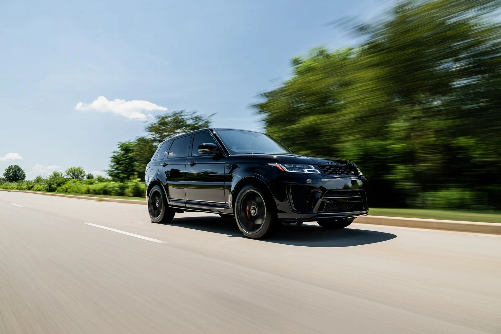 Black 2022 Range Rover Sport SVR driving along a tree-lined road, viewed from the front three-quarter angle.