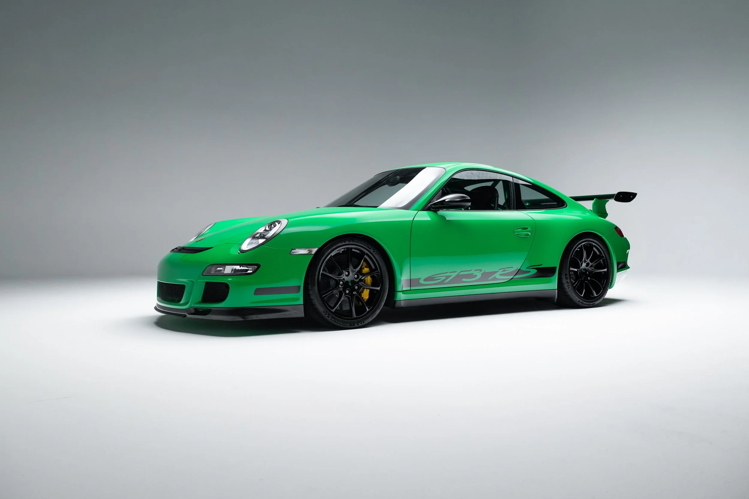 2008 Porsche 911 GT3 RS in green. Features a prominent rear wing, distinctive side graphics, and black alloy wheels with yellow brake calipers. Low stance enhances aerodynamic profile.