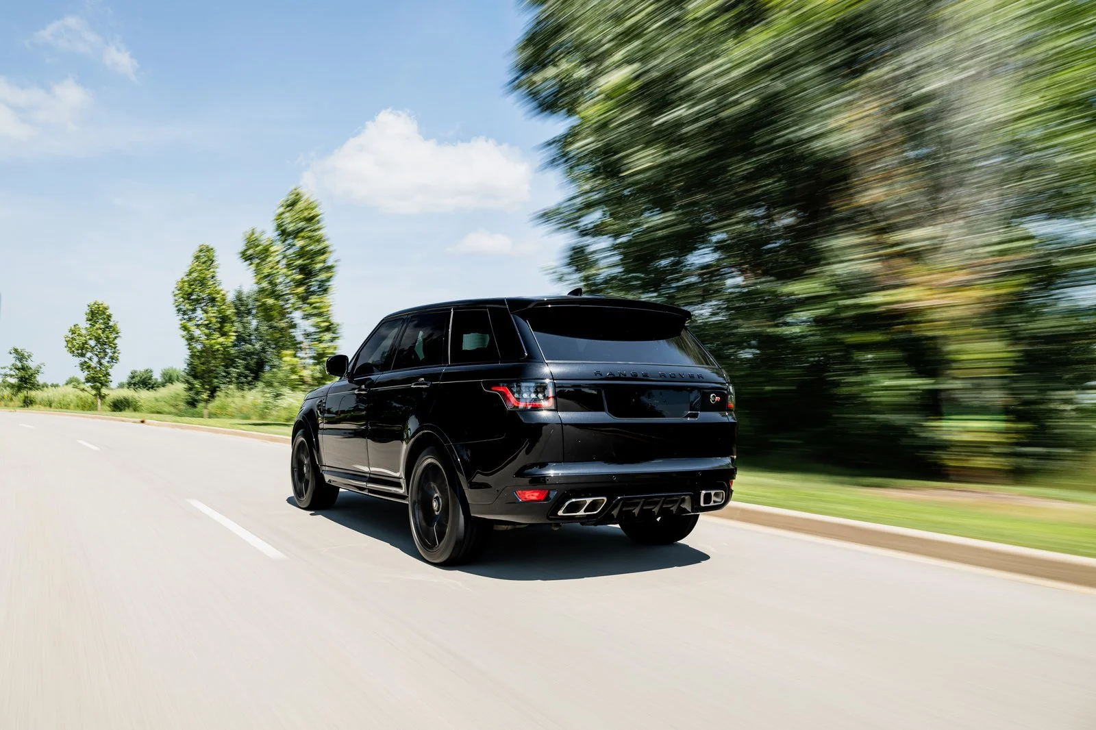 Rear three-quarter view of the black 2022 Range Rover Sport SVR driving along a tree-lined road.