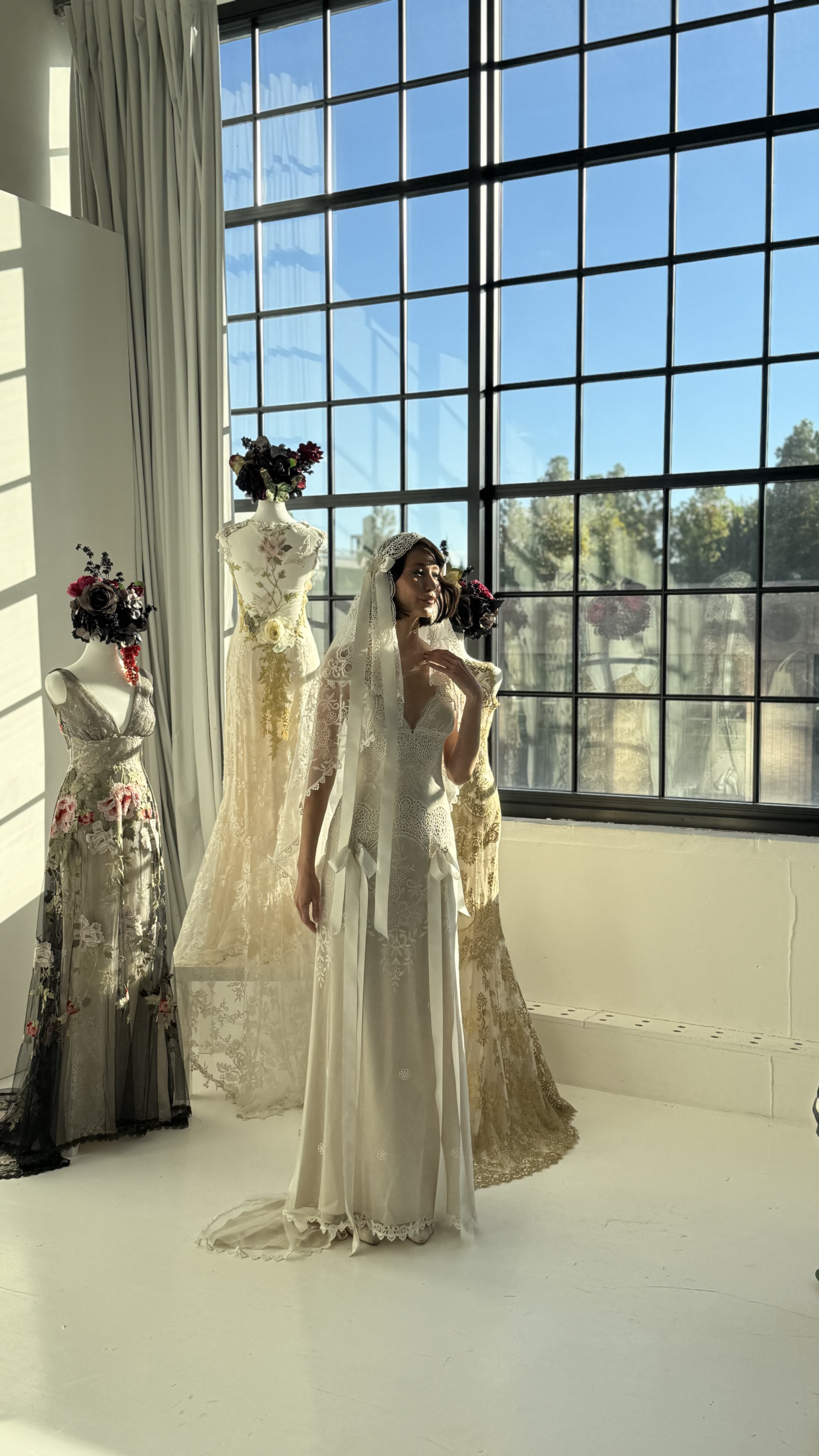 Bride in a lace gown and veil standing by a designer collection display at Daylight Studio's NYC bridal showroom venue
