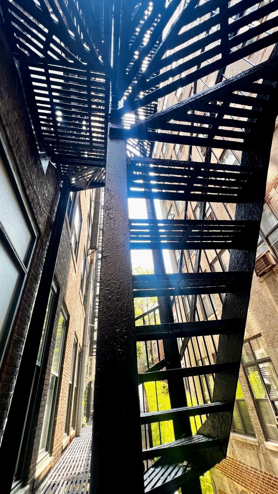 Fire escape stairs outside brick apartment building with metal railing, viewed from below.