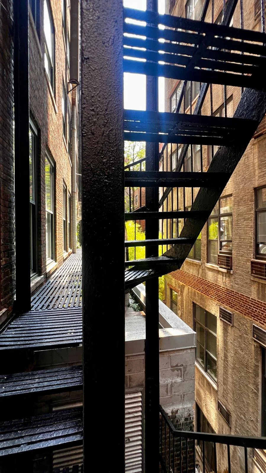 Exterior fire escape stairs on the side of a brick building between two adjacent buildings with metal railings and ladders.
