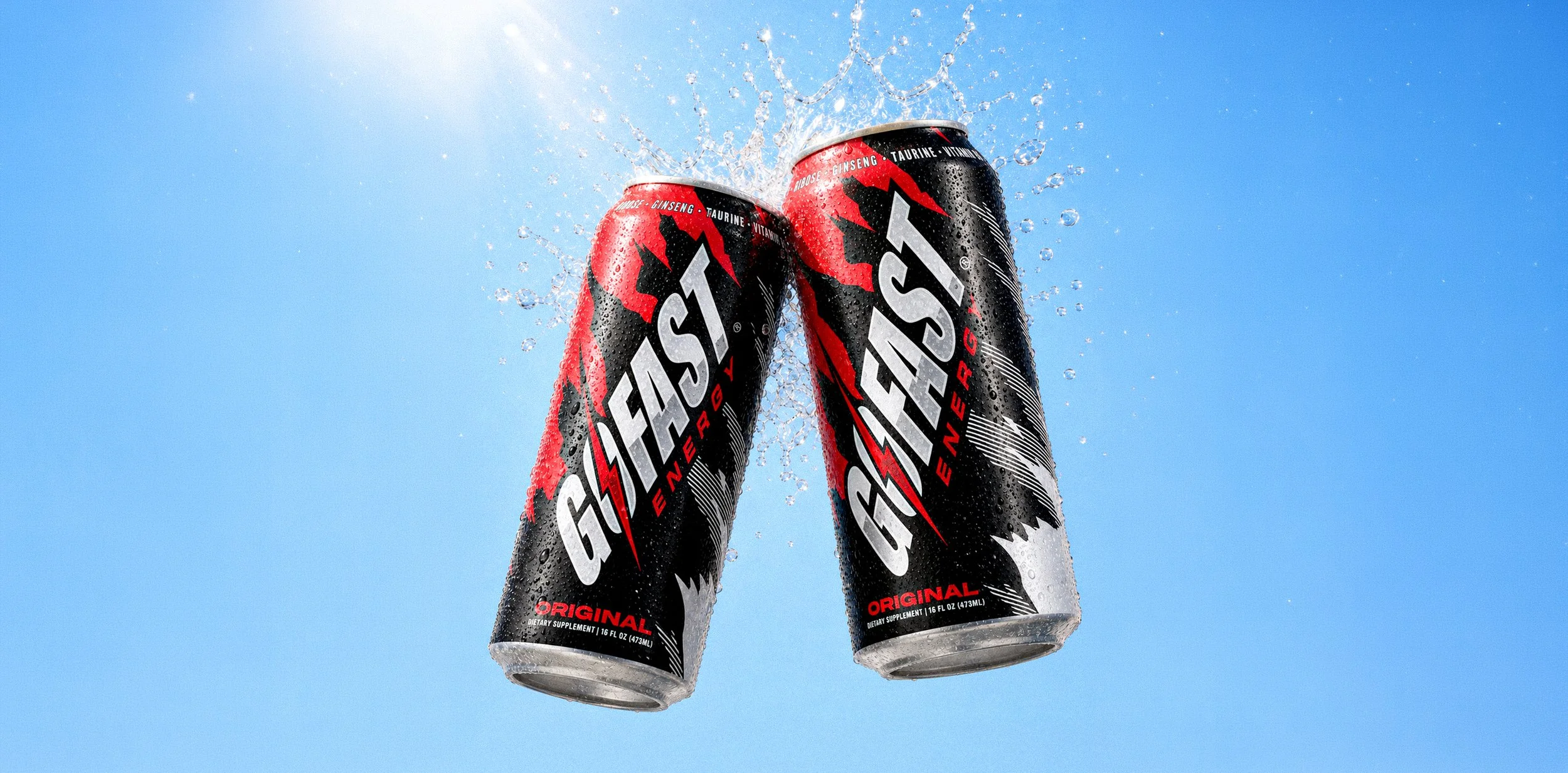 Two cans of GoFast® Energy in a black, red, and white design, spraying water against a blue sky.