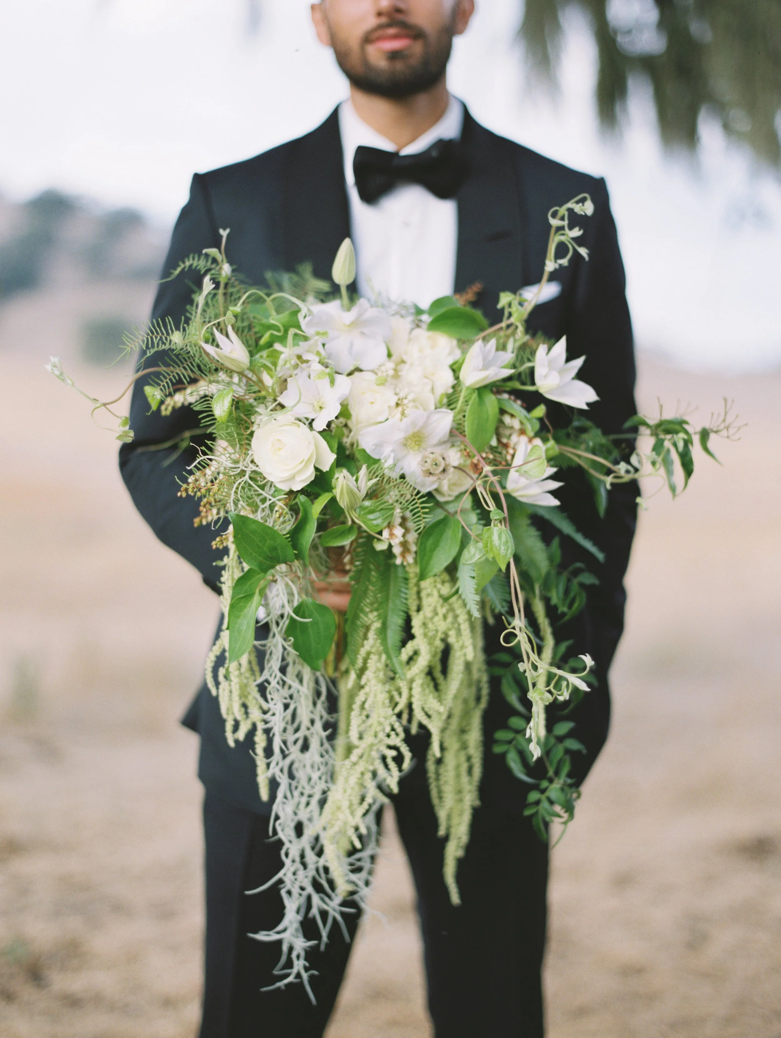 man in tuxedo holding lush greenery bouquet