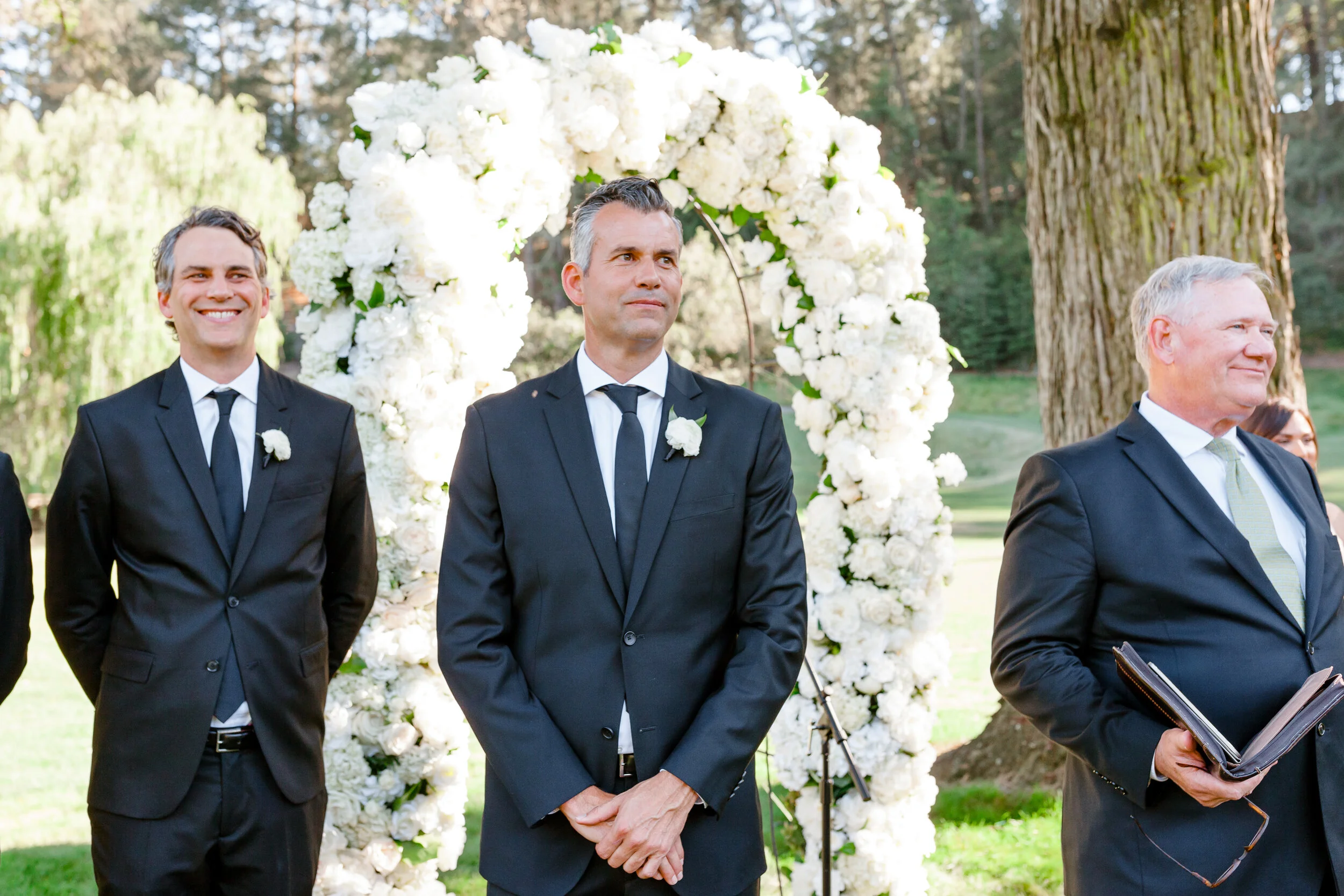 Groom stands before arch of white roses white hydrangeas white peonies image name: wedding-florist-boise-629