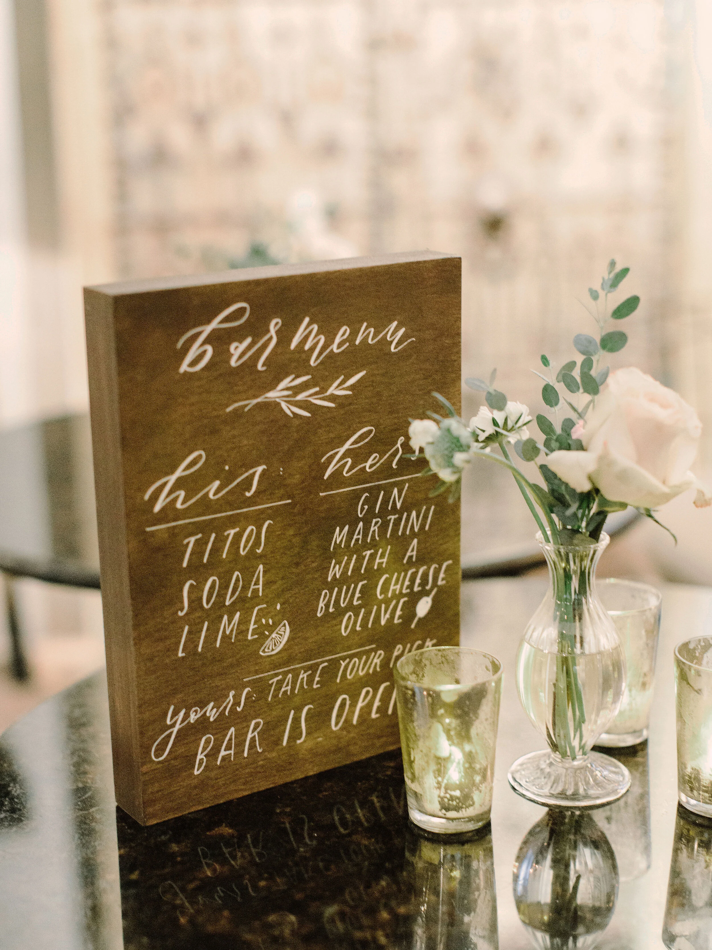 Wooden bar menu sign sits next to single white rose image name: wedding-florist-boise-746