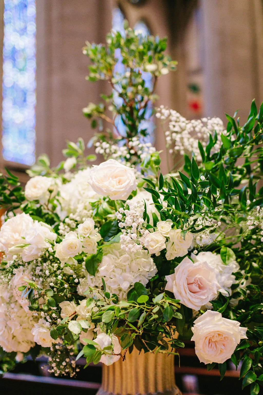 Floral arrangement white roses hydrangeas baby's breath surrounded green leaves. Image name: wedding-florist-boise-54