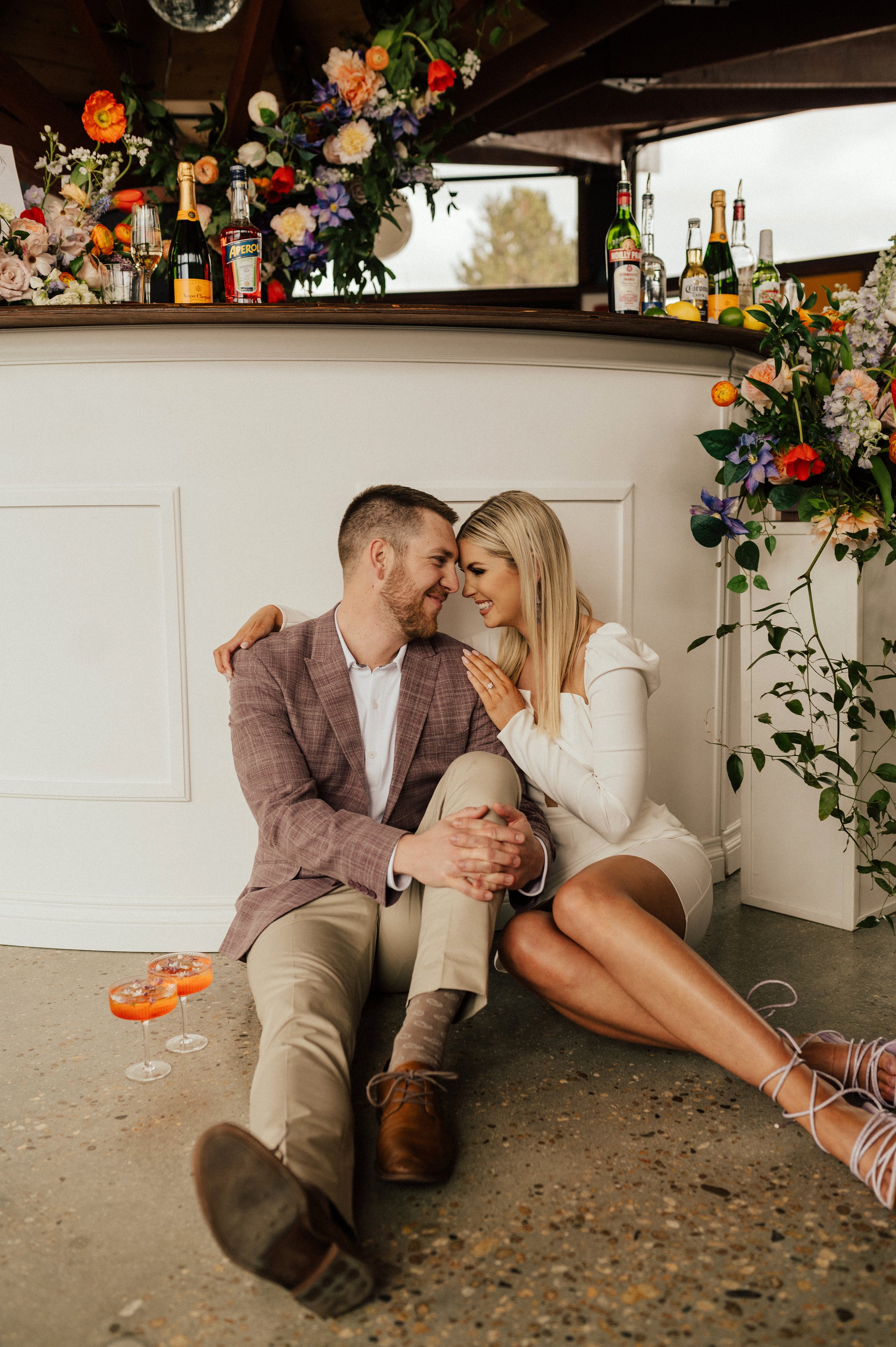 Couple sitting in front of bar surrounded by poppies tulips cosmos ranunculus lilacs image name: wedding-florist-boise-258