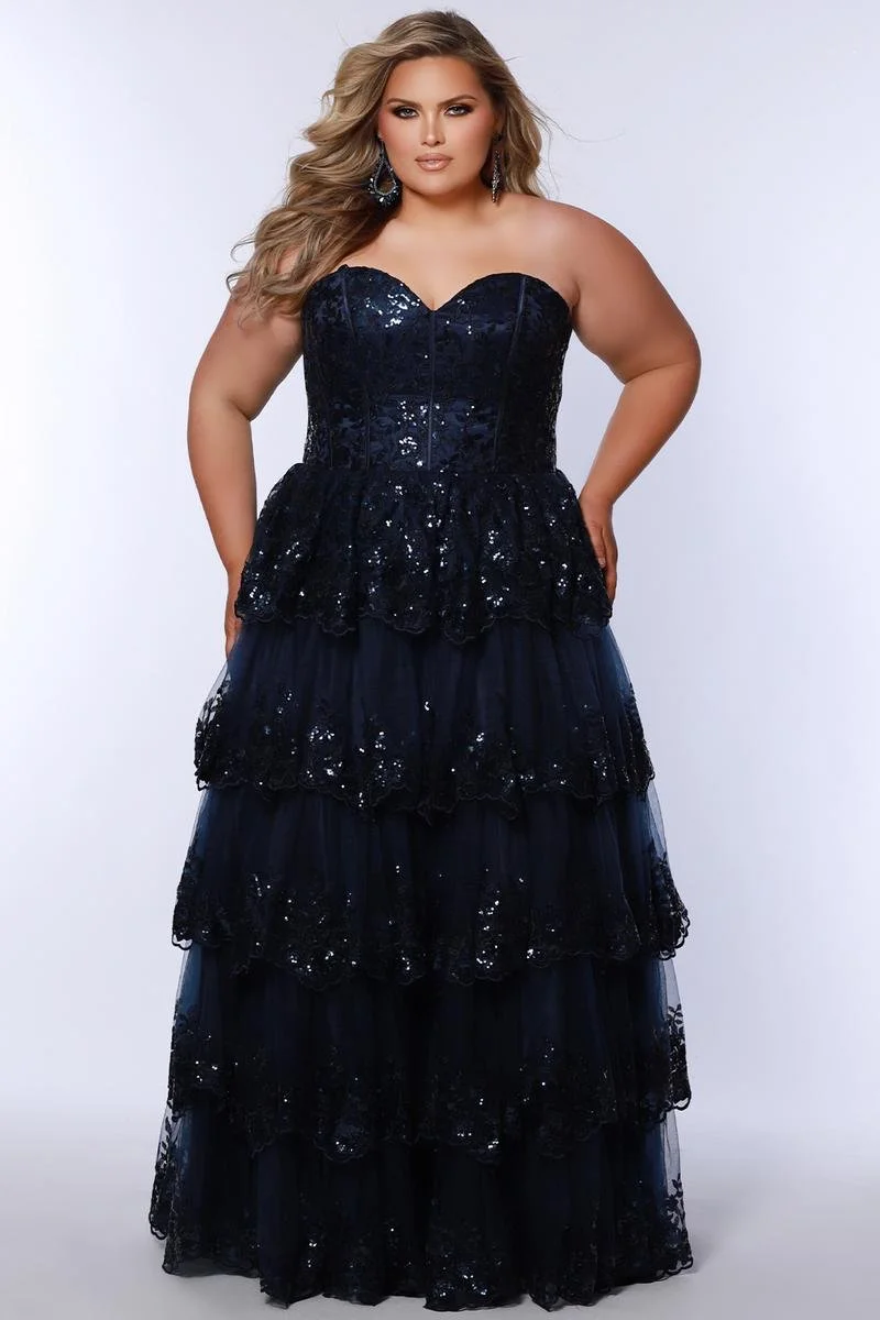 A woman with long curled hair and evening makeup wears a black sequin covered strapless gown with a layers of ruffles in the skirt.
