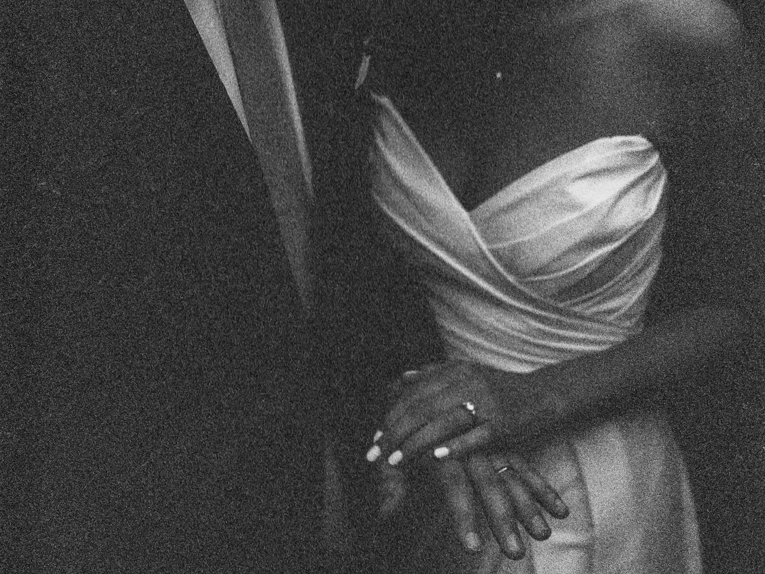 Black and white photo of a woman wearing a striped shirt, standing with her hand on her hip, in a dark environment.