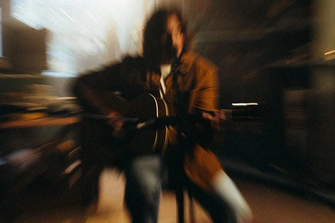 Person playing an acoustic guitar in a dimly lit room.