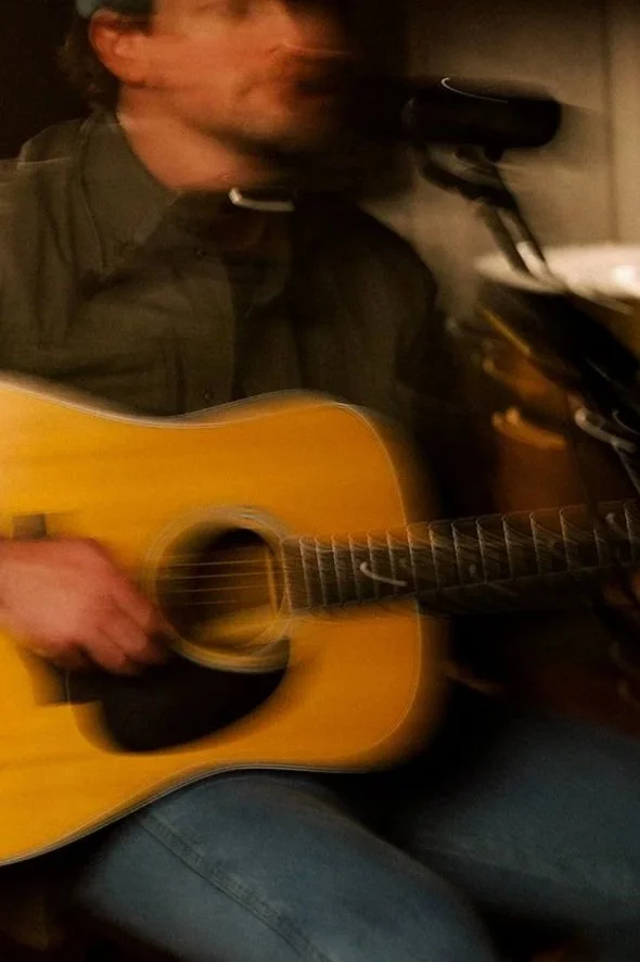 A man playing an acoustic guitar while singing into a microphone.