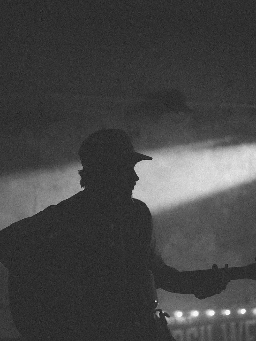 Silhouette of a person playing guitar in a dark setting with a light beam illuminating the background.