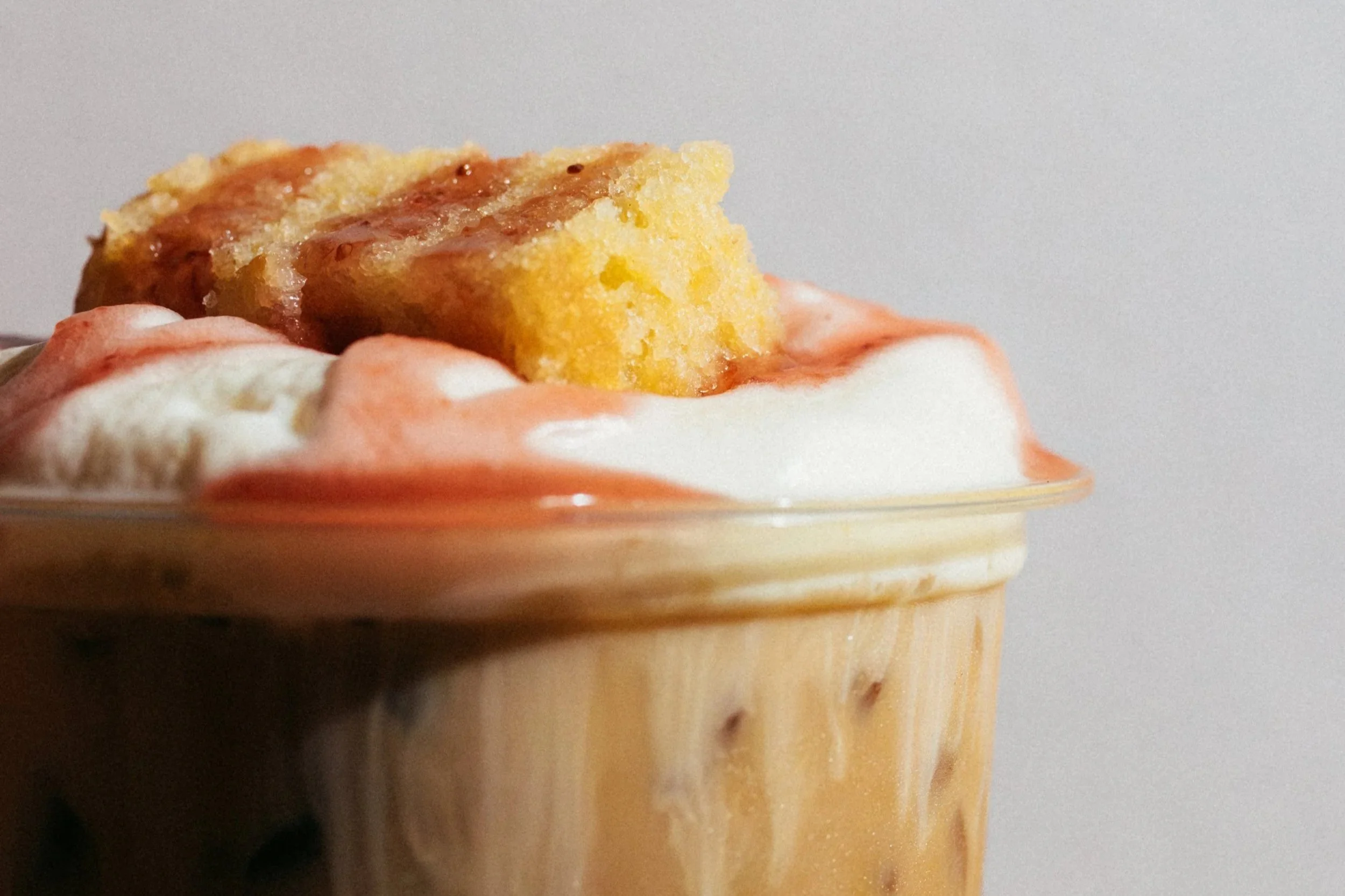 A close-up of a slice of vanilla cake with strawberry jam and whipped cream on top, served on a glass dish. Cafe Stai Manso