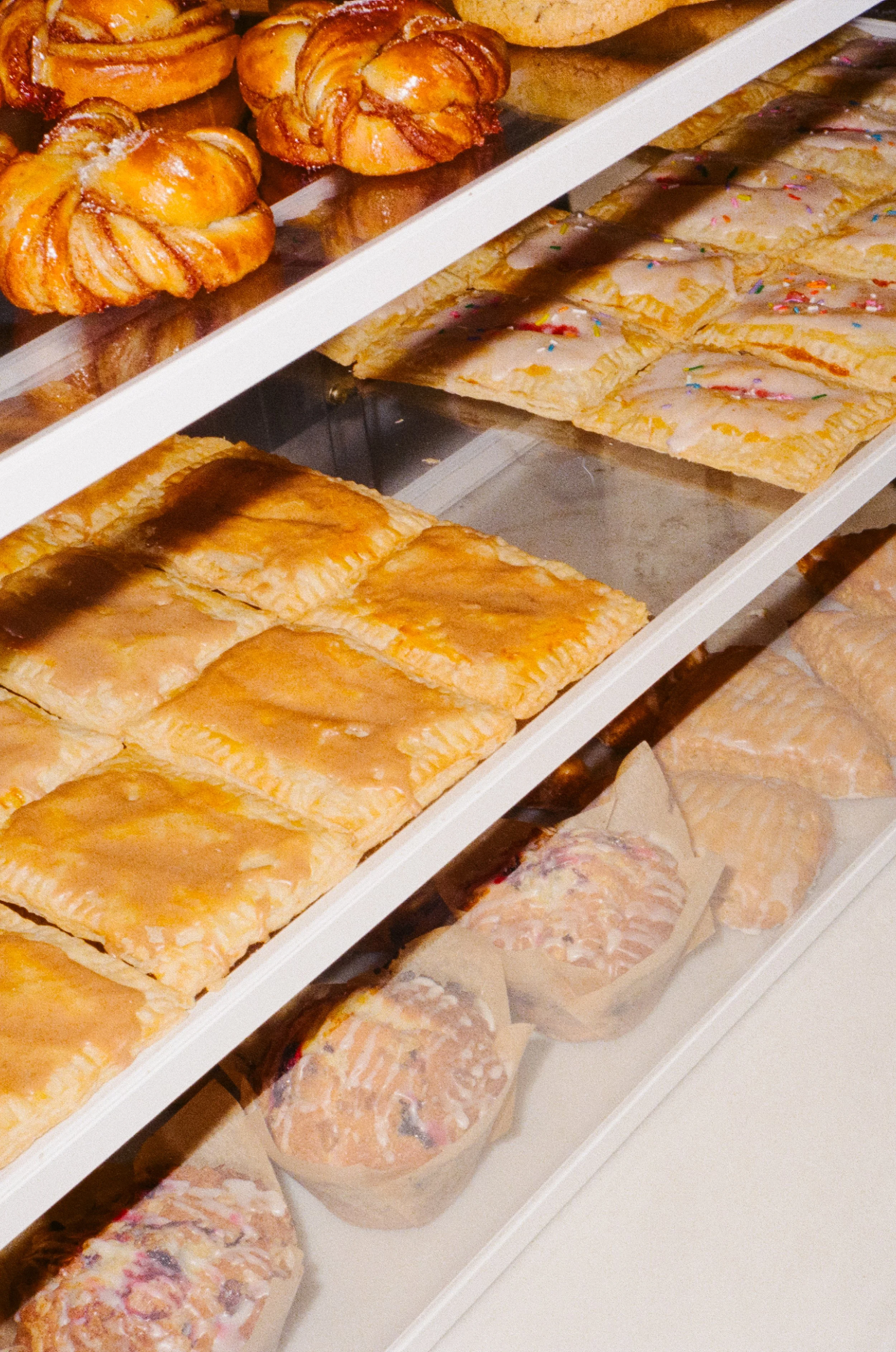 A display case with various baked goods including croissants, frosted pastries with sprinkles, and muffins.