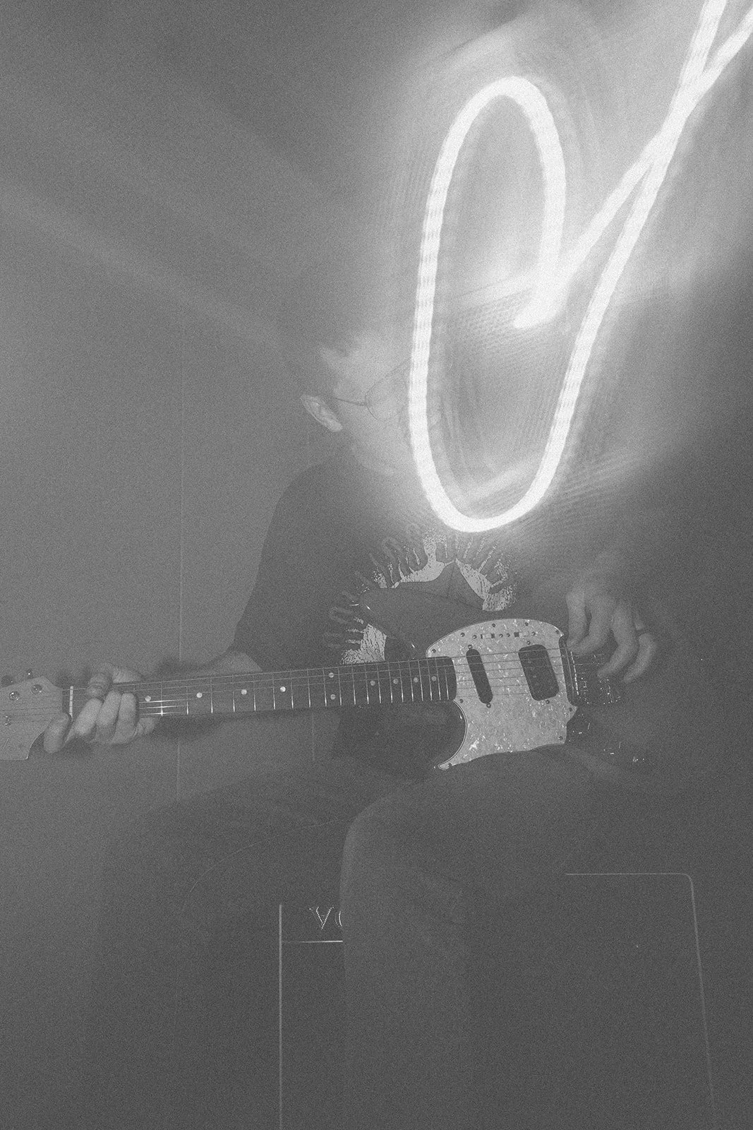 Person playing electric guitar in front of a neon 'O' sign, echoing in black and white.