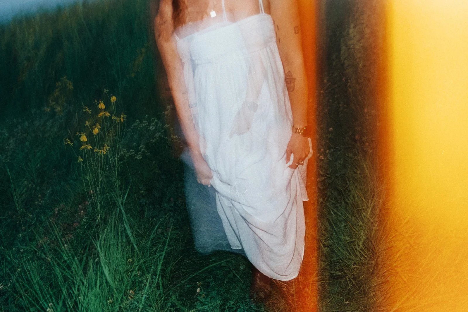 A person dressed in white with a watch and rings standing outside near a green field.