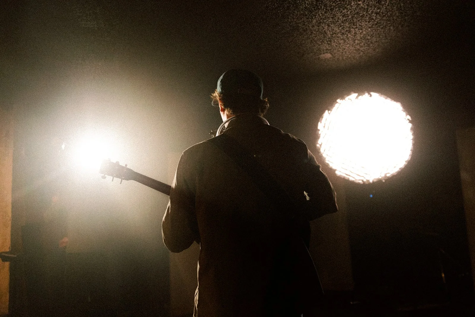 Person with guitar facing bright lights in a dark room.