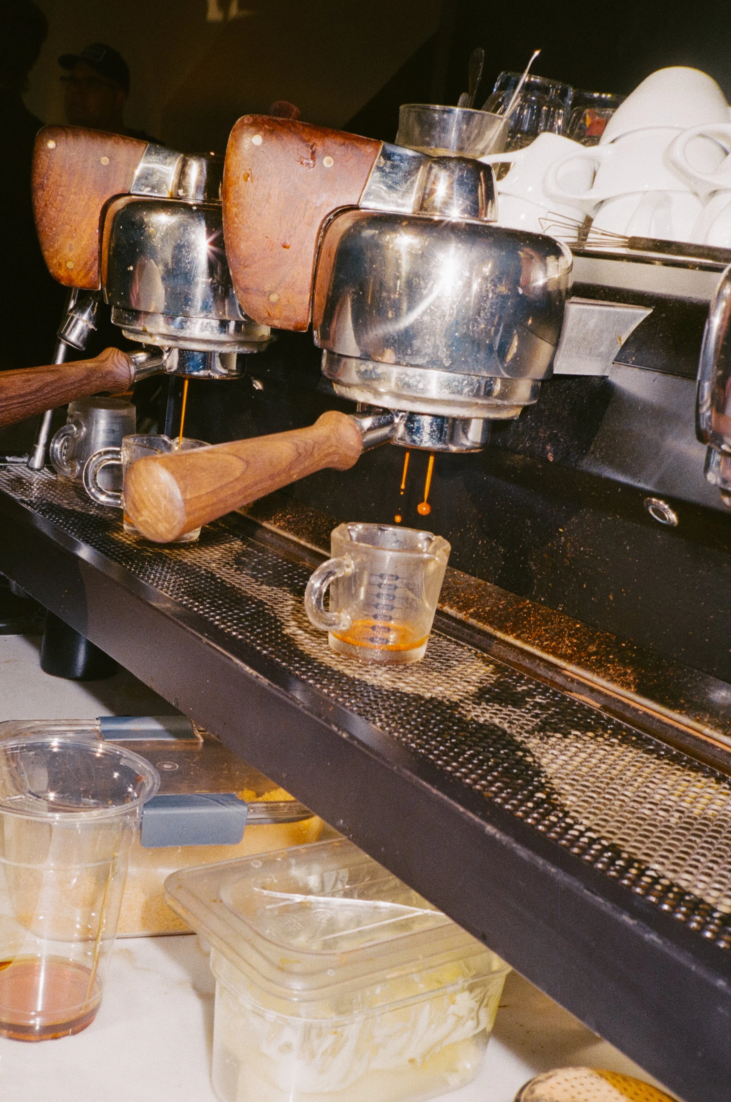 Espresso machine brewing coffee into small glass cups, with spilled coffee on the tray and lower surface.