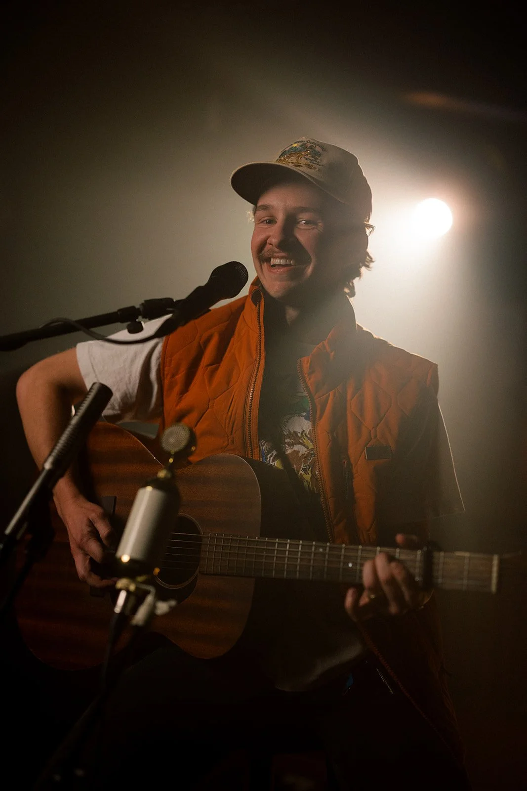 Man playing guitar and singing into a microphone with bright backlighting and smile.