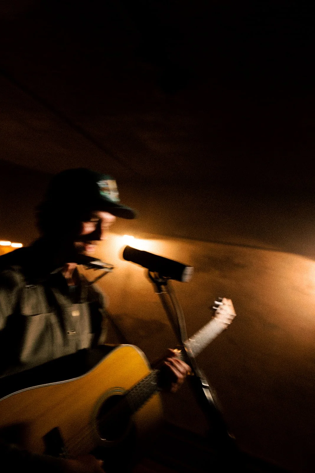 A person playing guitar and singing into a microphone on dimly lit stage.