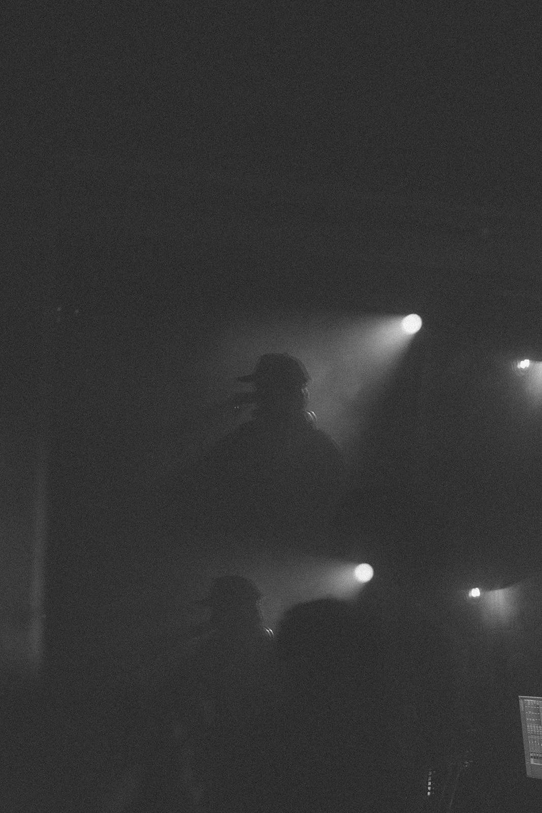 Silhouette of a person wearing a hat, performing on stage with stage lights shining in the background, in black and white.
