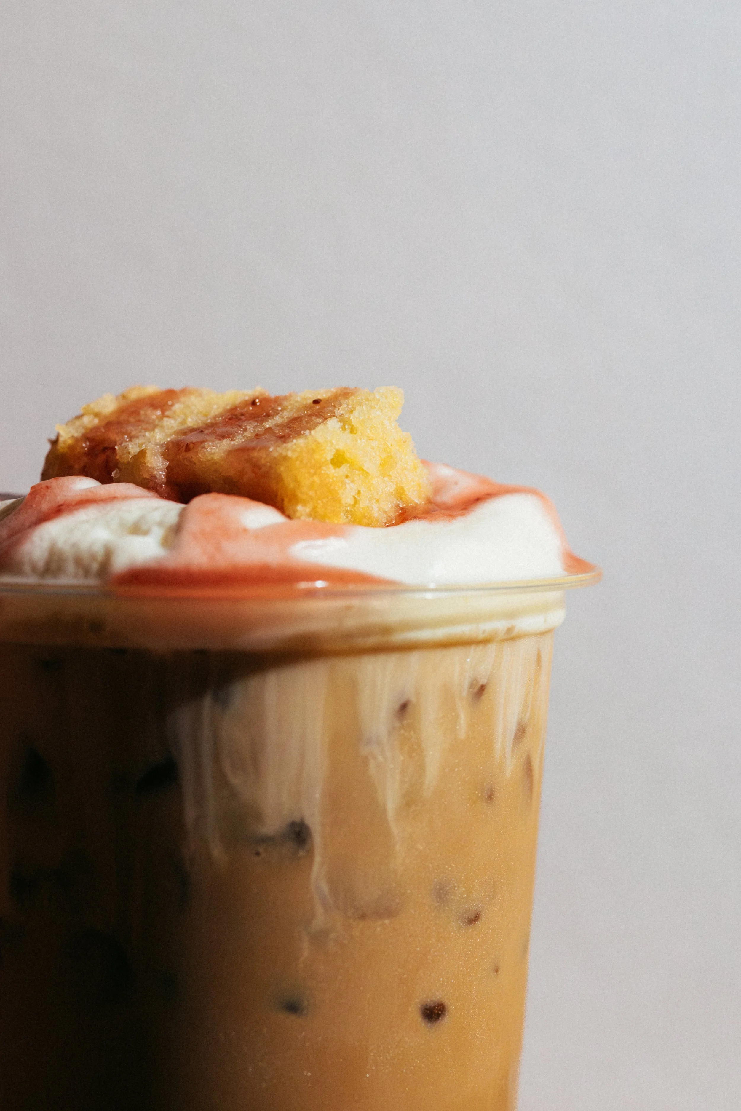 Close-up of a frosted glass containing an iced coffee with whipped cream and a piece of yellow cake with icing on top. Cafe Stai Manso