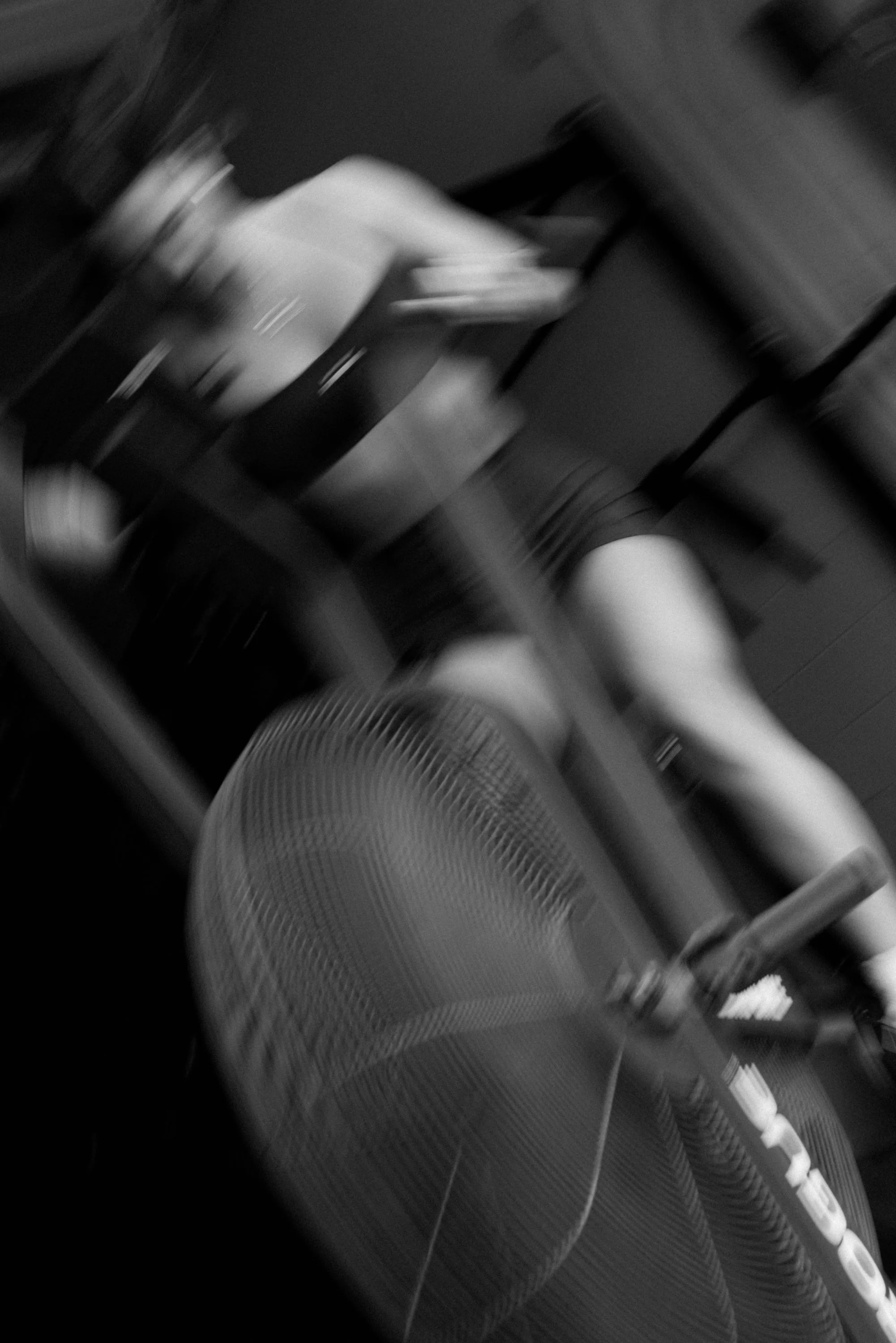 A blurry black and white photo of a person sitting on a chair. The person's legs are visible, and they are holding an object.