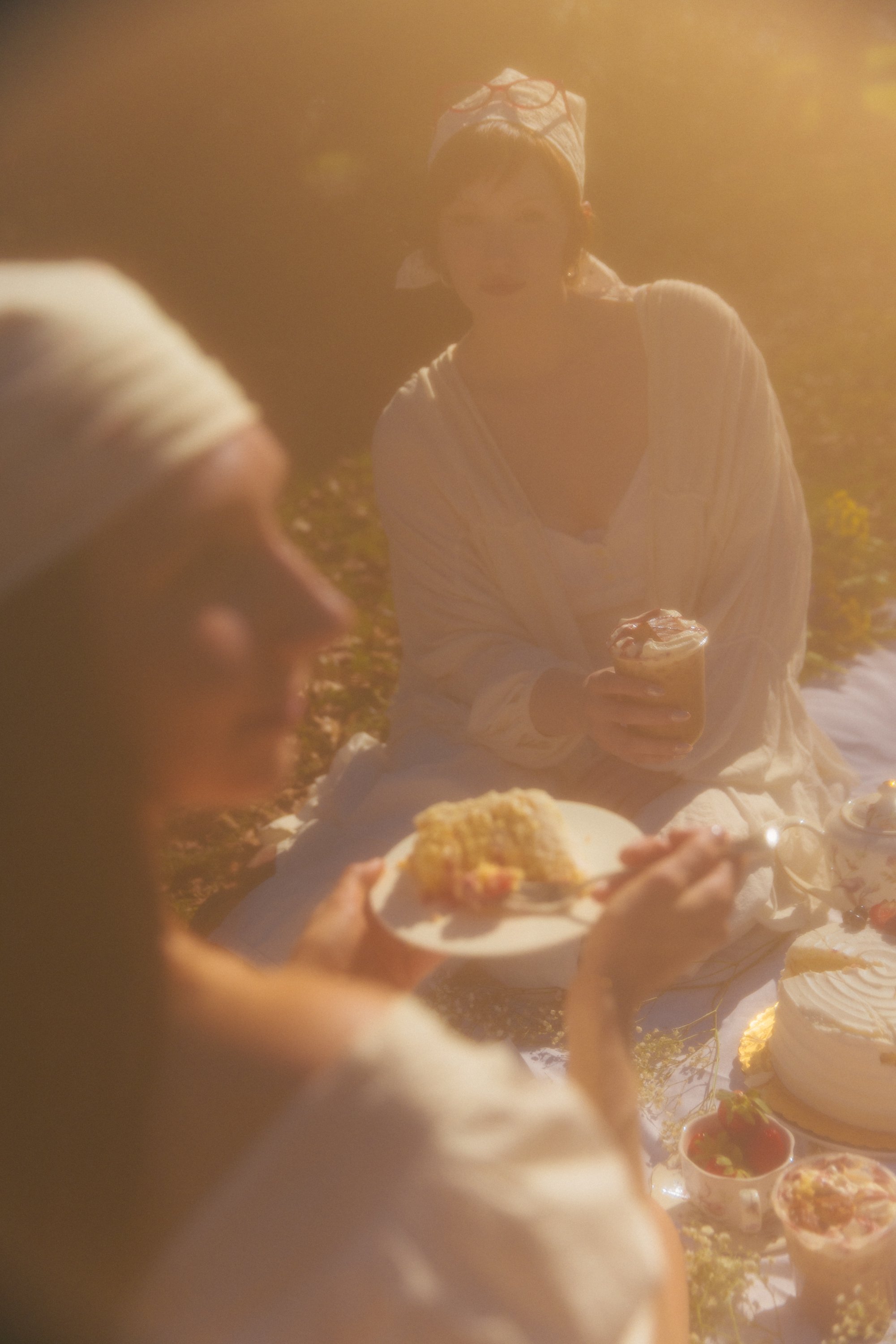 People enjoying a picnic outdoors with food, desserts, and drinks on a sunny day.