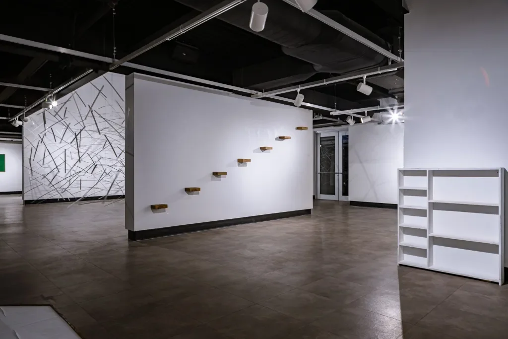 Empty art gallery with white walls, wooden shelves on wall, and white bookshelves on floor, modern lighting, and minimal decor.