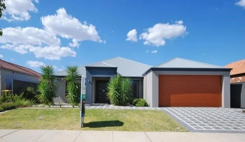 Modern house with a gray roof and walls, featuring a wooden garage door, front yard with green grass and plants, and a blue sky with white clouds.