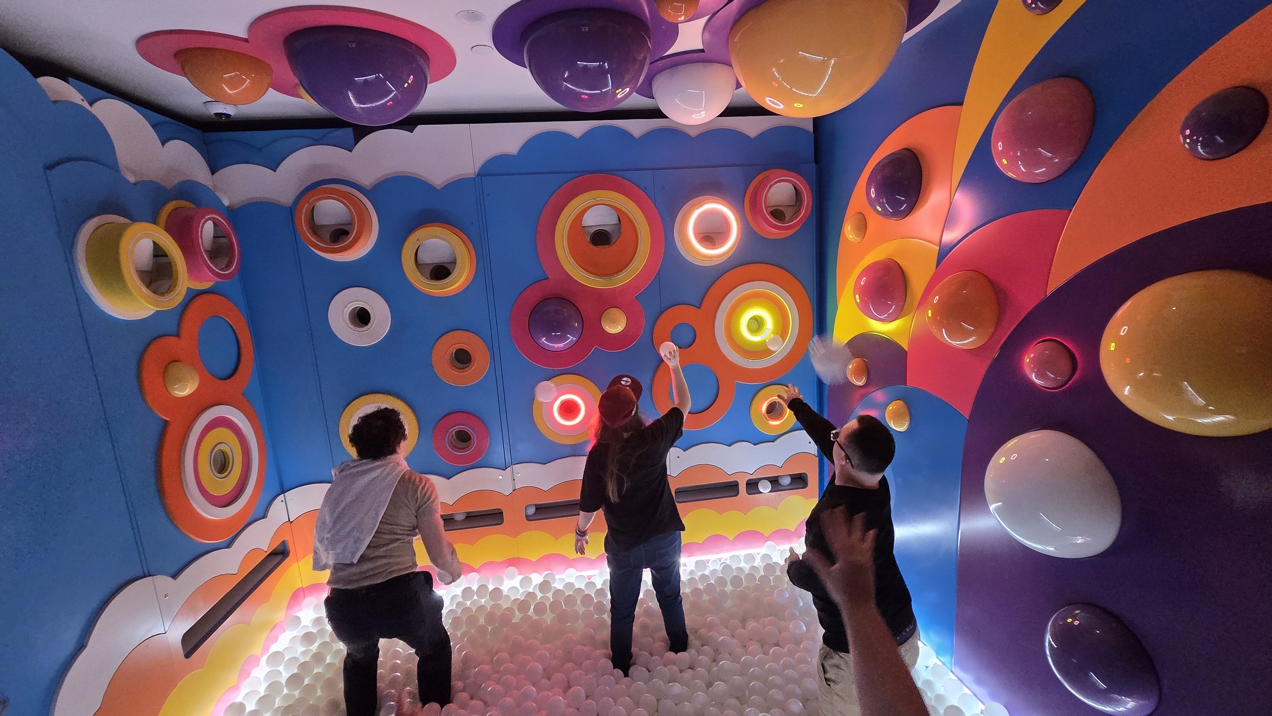 People playing in an indoor ball pit with colorful walls and circular decorations.