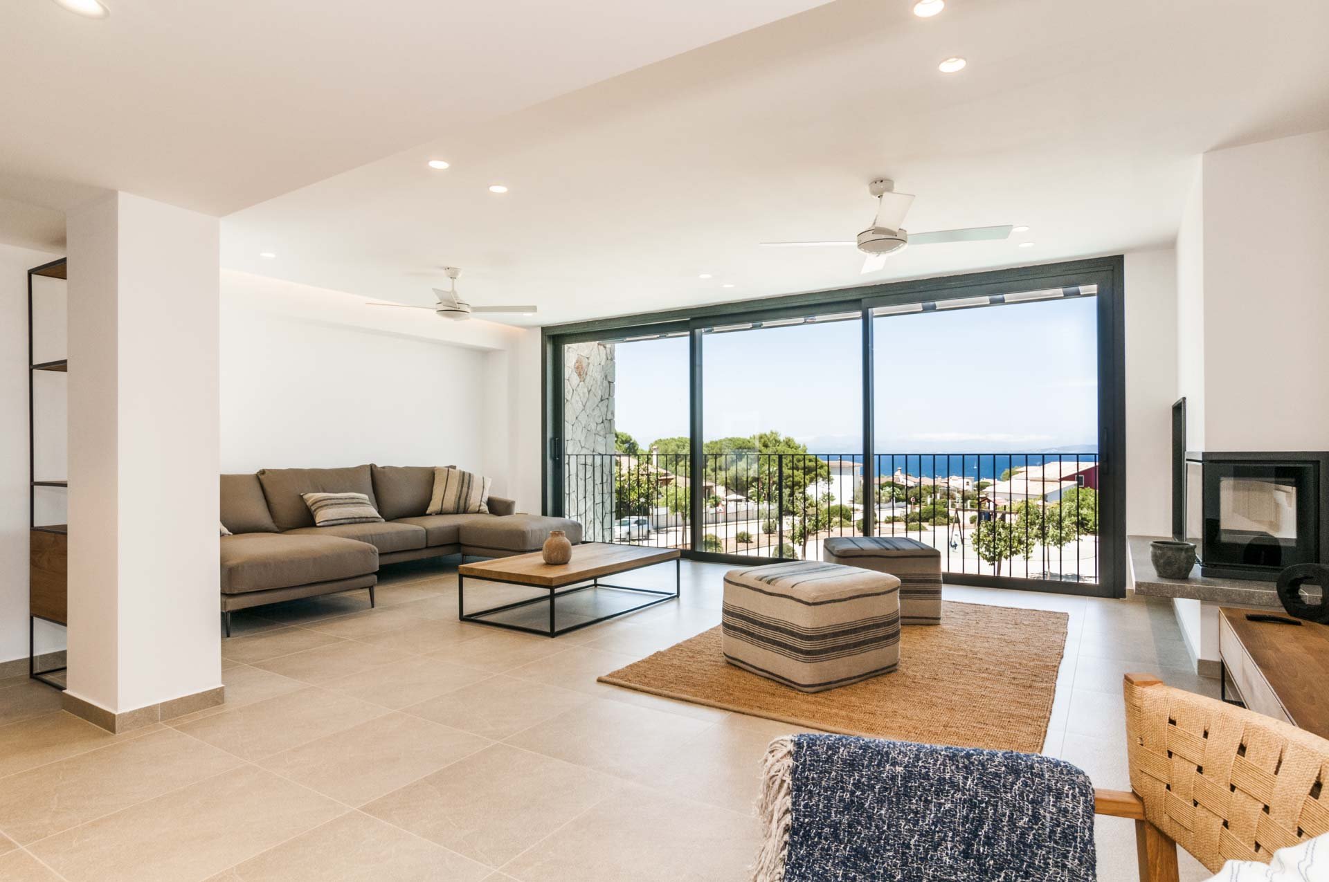 Modern living room with large windows, beige sectional sofa, wooden coffee table, and ocean view.