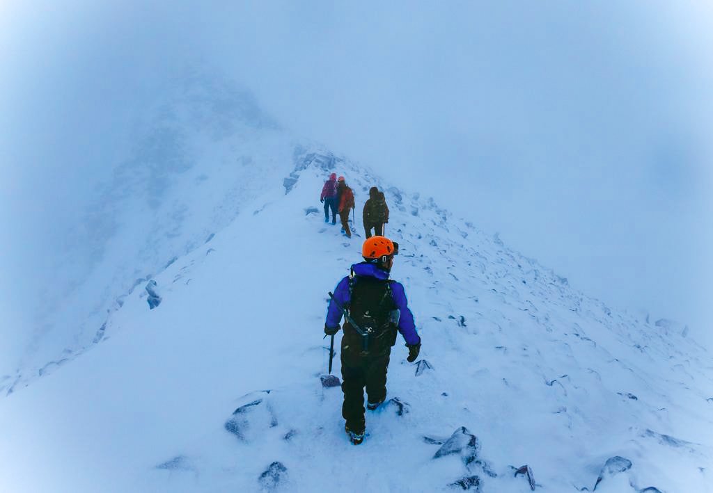 Group of climbers making their way up a snowy mountain ridge in foggy weather.