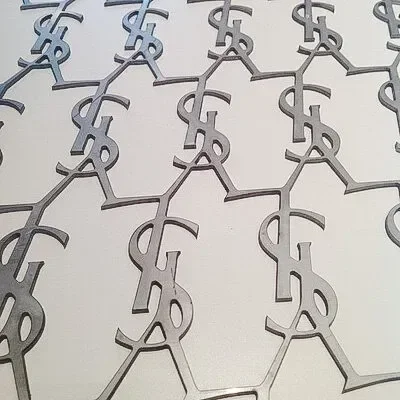 Repeating metallic YSL monograms arranged in rows on a pale surface
