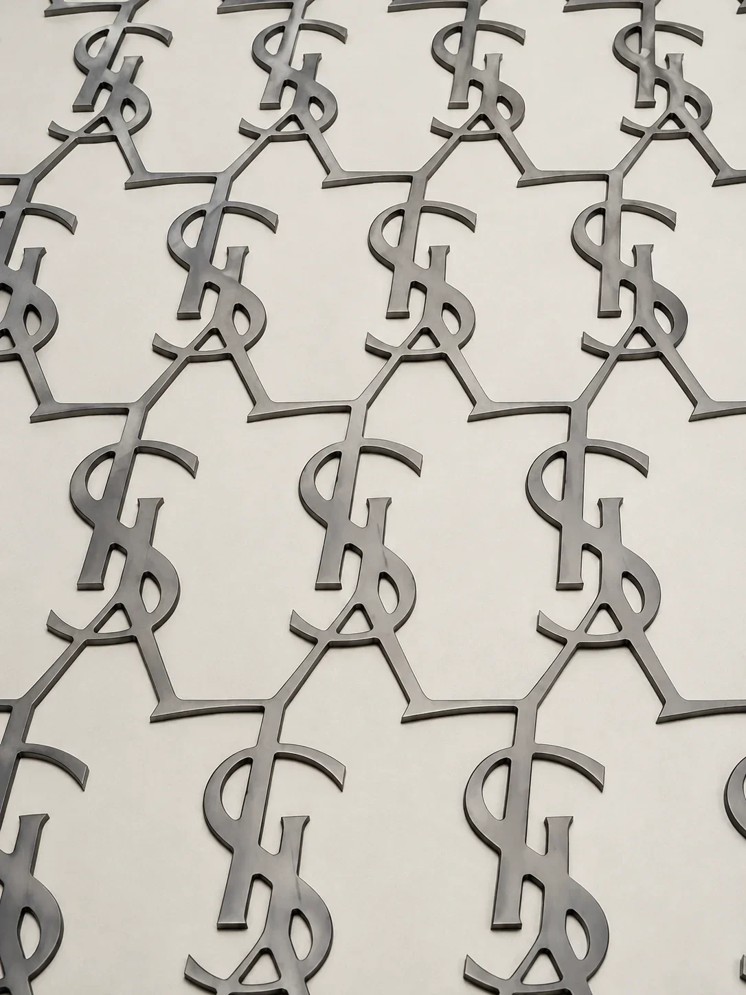 Waterjet-cut metal YSL monograms arranged in a repeating pattern for a luxury retail interior.