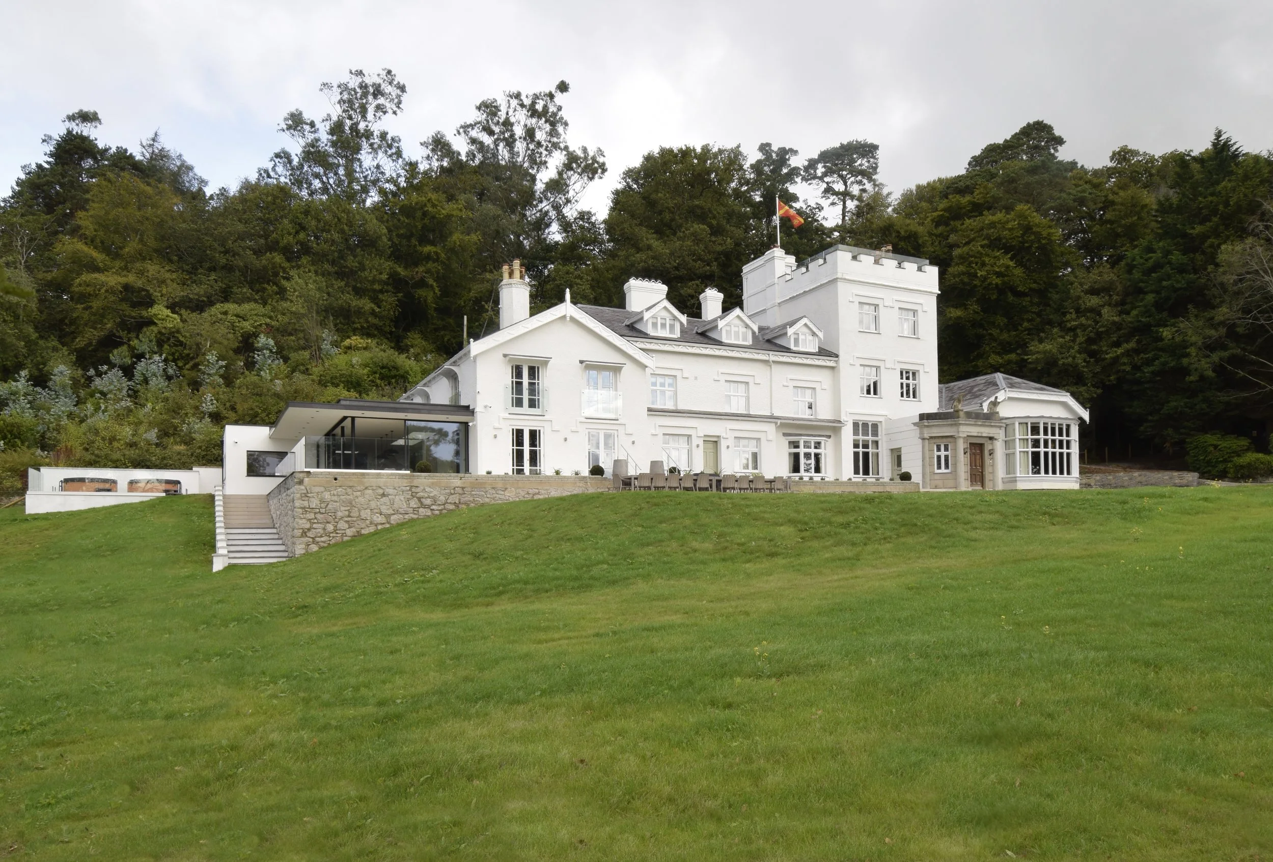 A large white house on a hill with a green lawn in front and trees in the background.