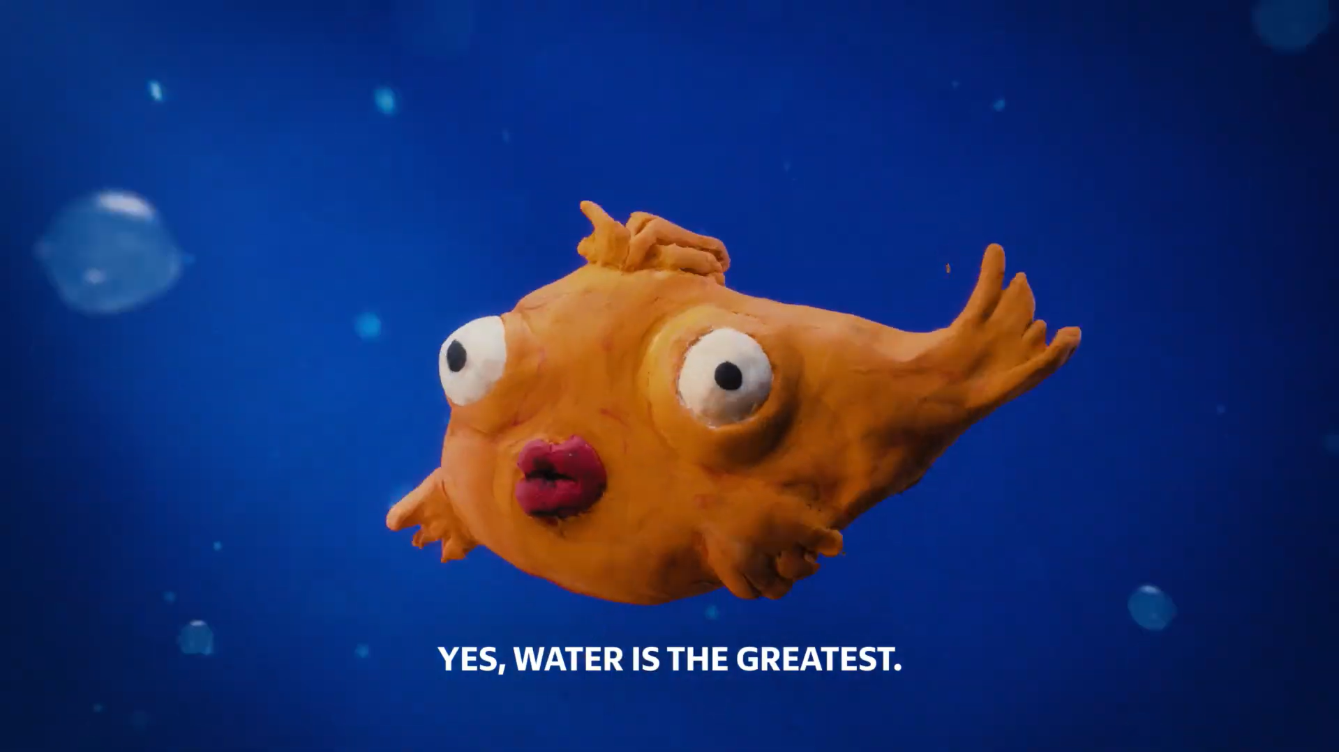 Clay fish with wide eyes floats underwater against a deep blue background.