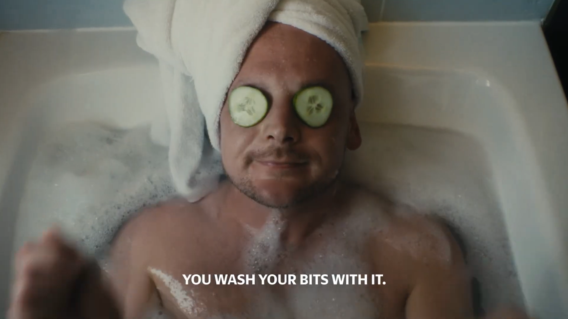 Man relaxes in a bath with cucumber slices over his eyes.